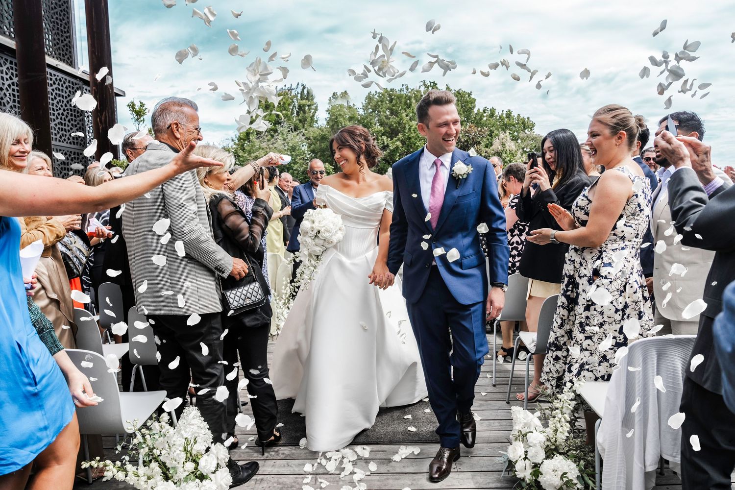 Wedding guests joyfully throw confetti over the newlyweds during an outdoor ceremony celebration.