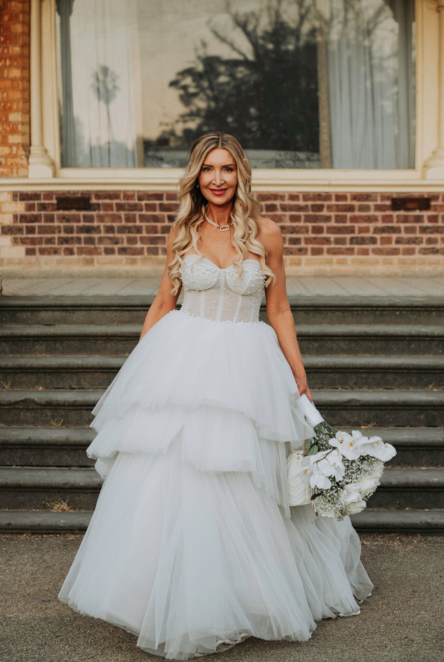 A bride in a layered tulle wedding gown poses gracefully on stone steps at sunset.