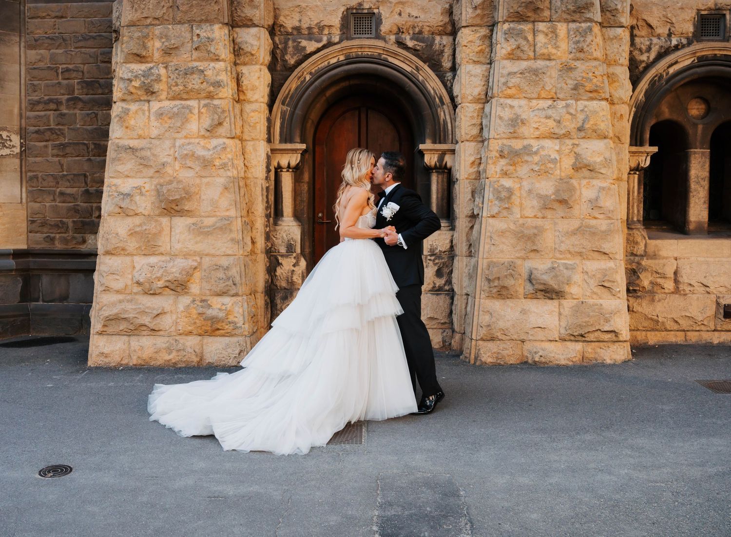 A bride in a flowing white wedding gown walks gracefully through an elegant stone archway.