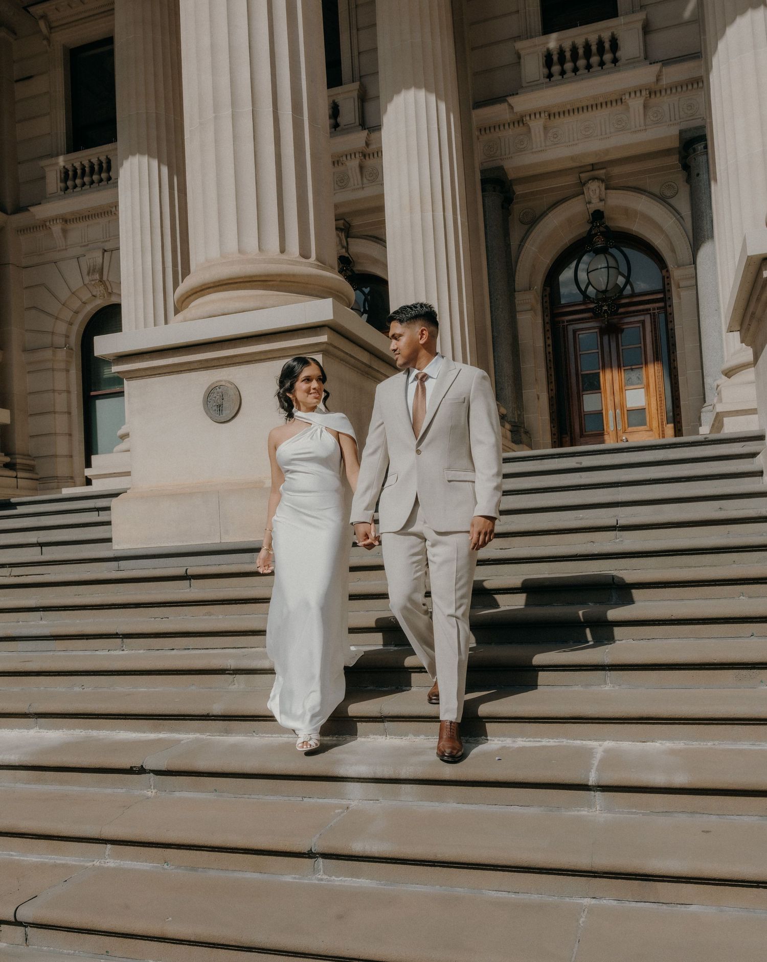 A couple in wedding attire sits on grand marble steps of a classical building in a romantic sequence of photos.