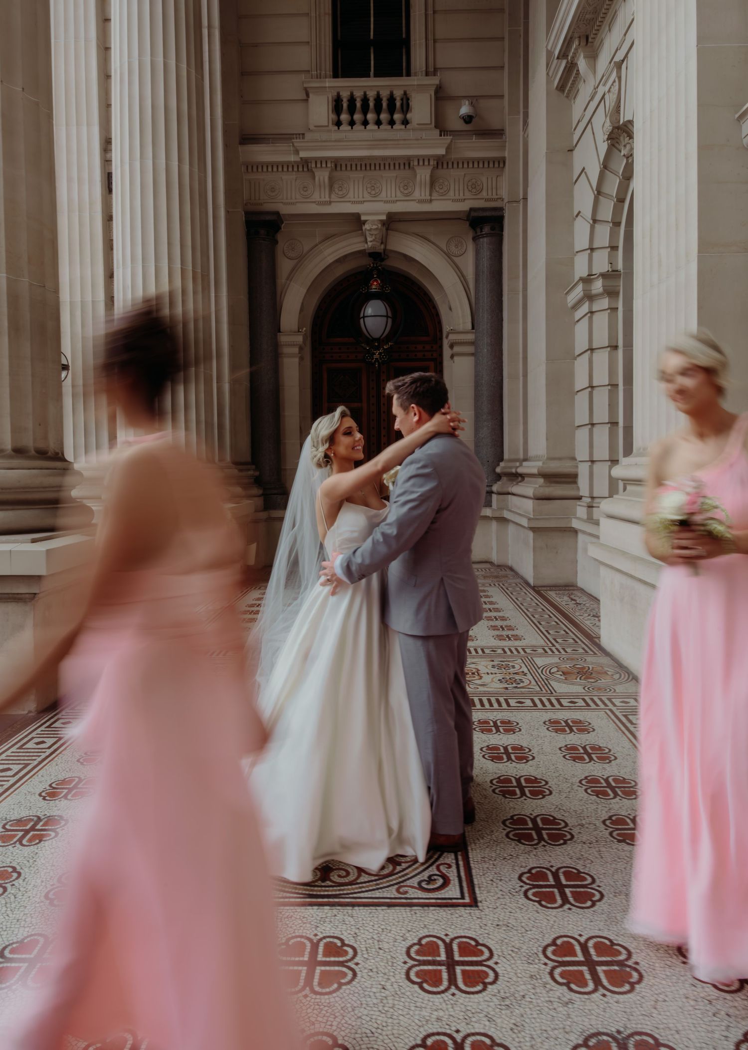 Wedding couple shares a romantic dance in an elegant hallway with bridesmaids in pink dresses creating a motion blur effect.