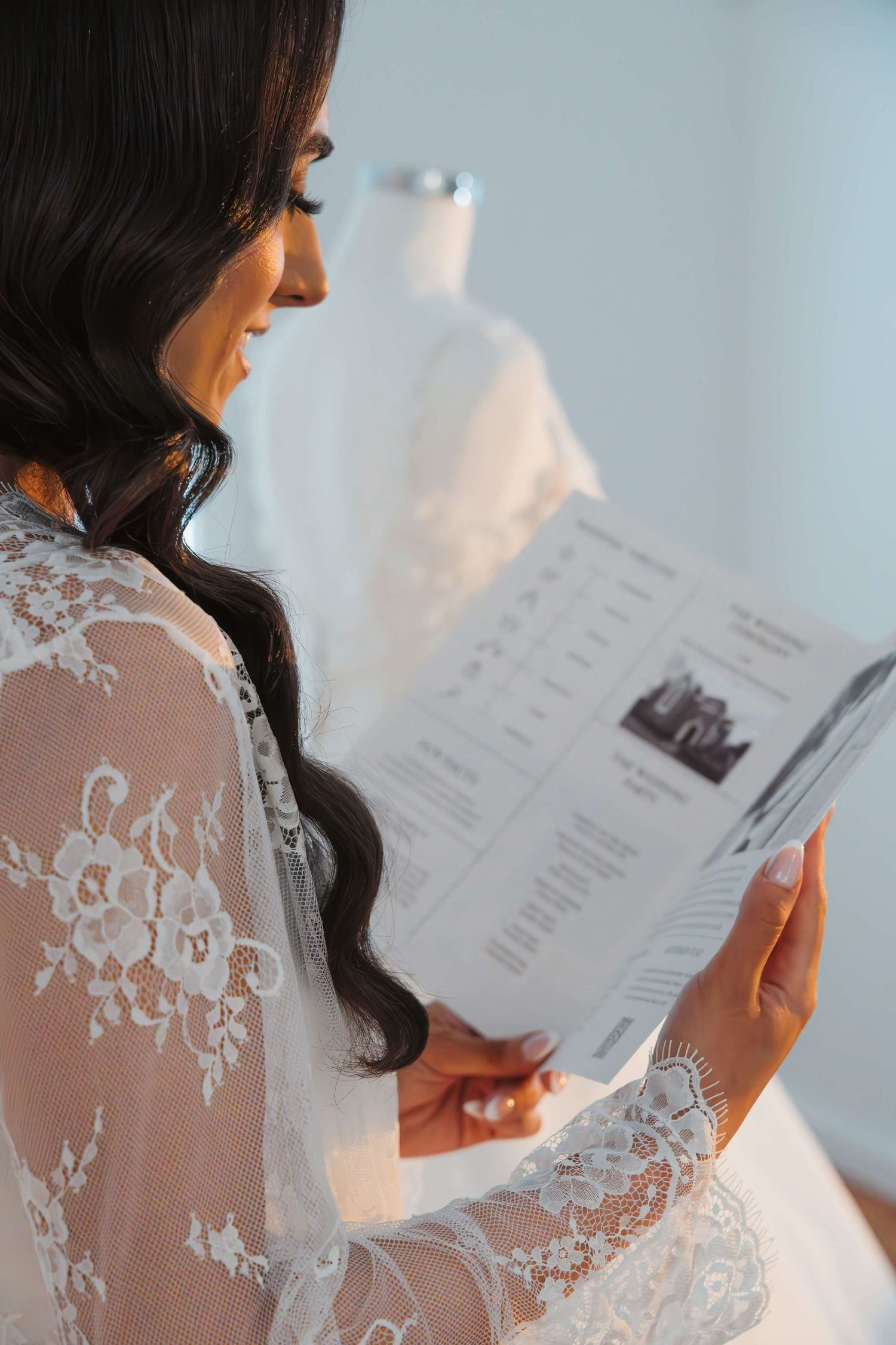 A person wearing a delicate white lace robe reads a document in side profile against a bright background.