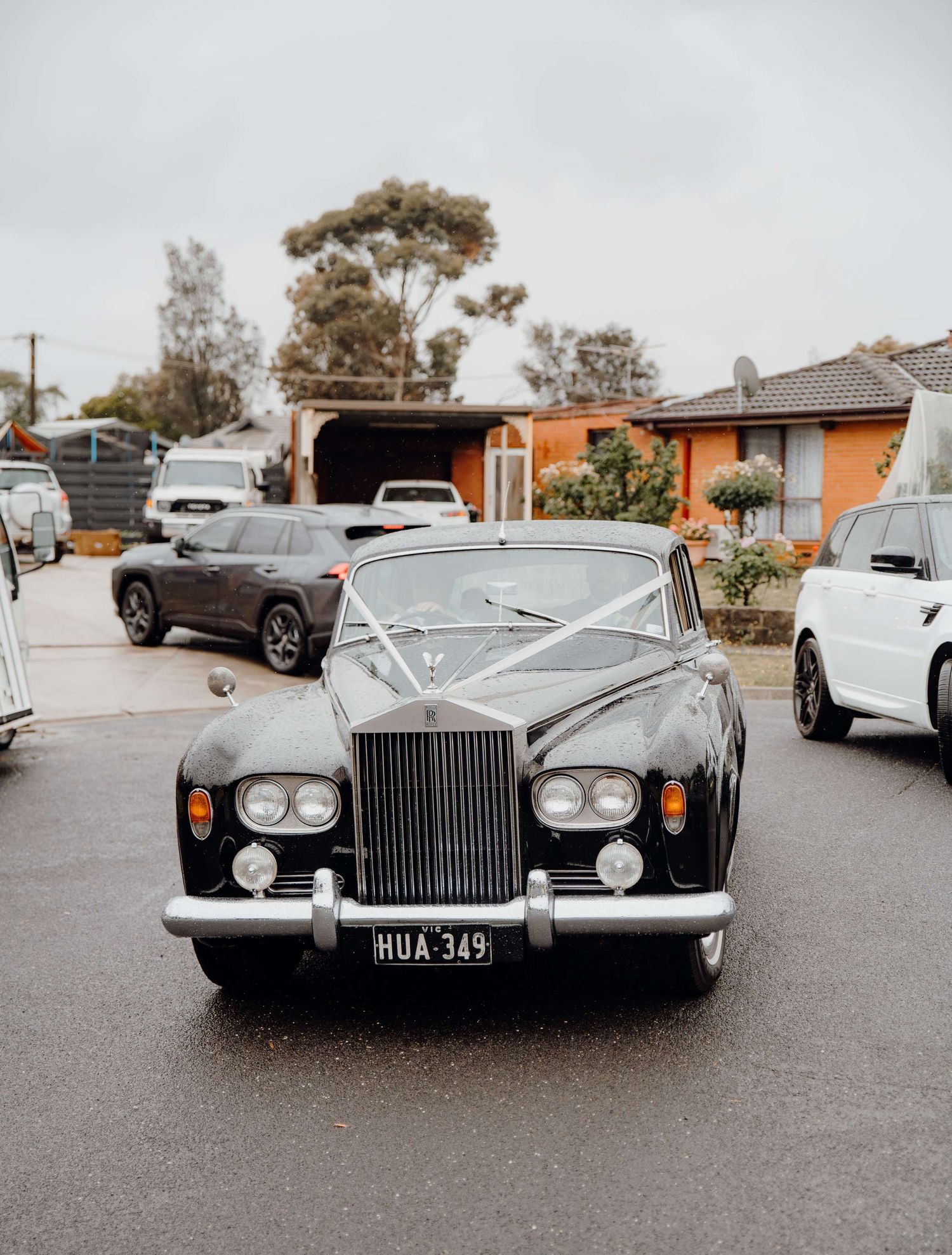 Classic Rolls-Royce luxury car parked on suburban street with modern vehicles in background.