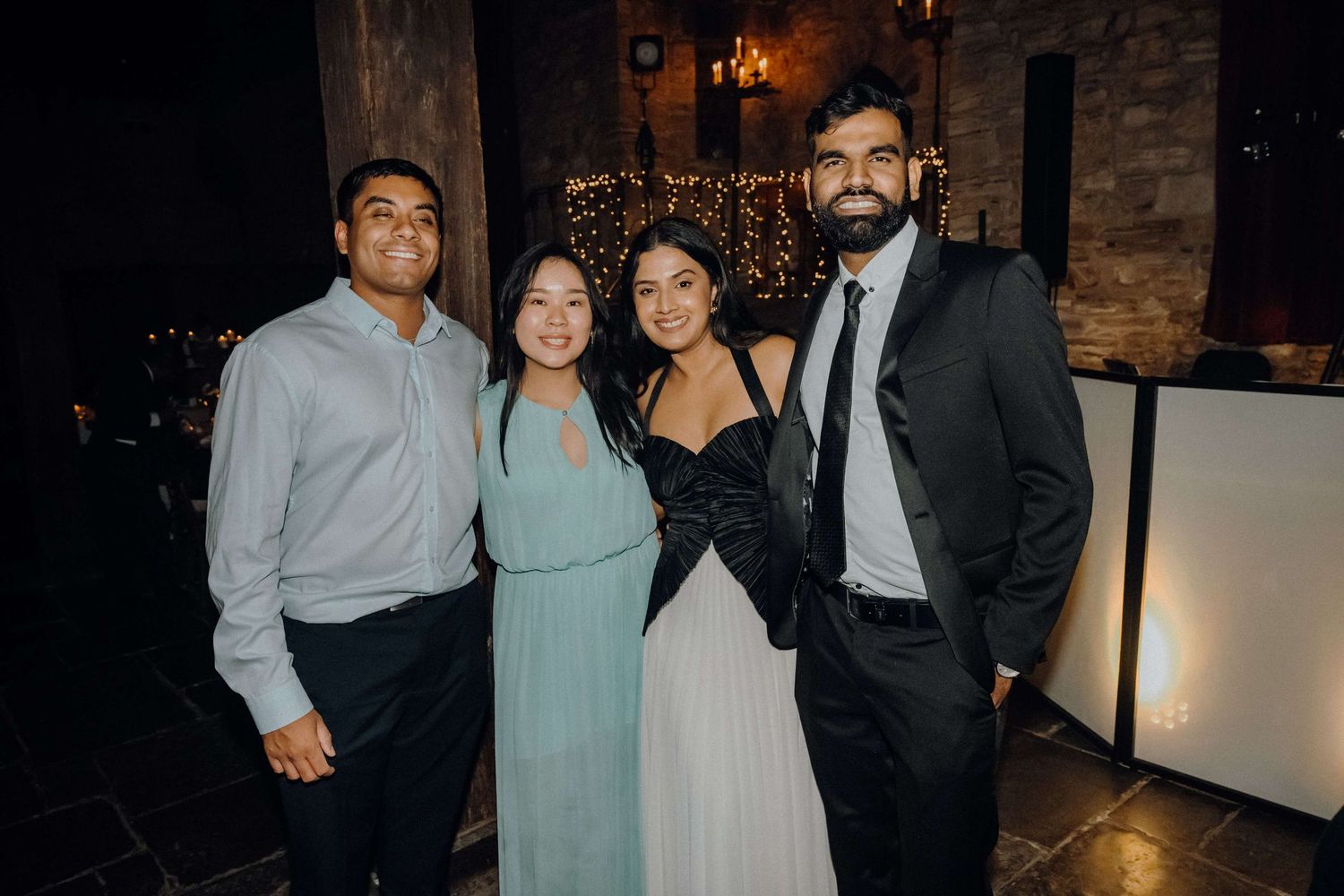 Group of friends pose together at an evening event in a rustic brick-walled venue with warm lighting.