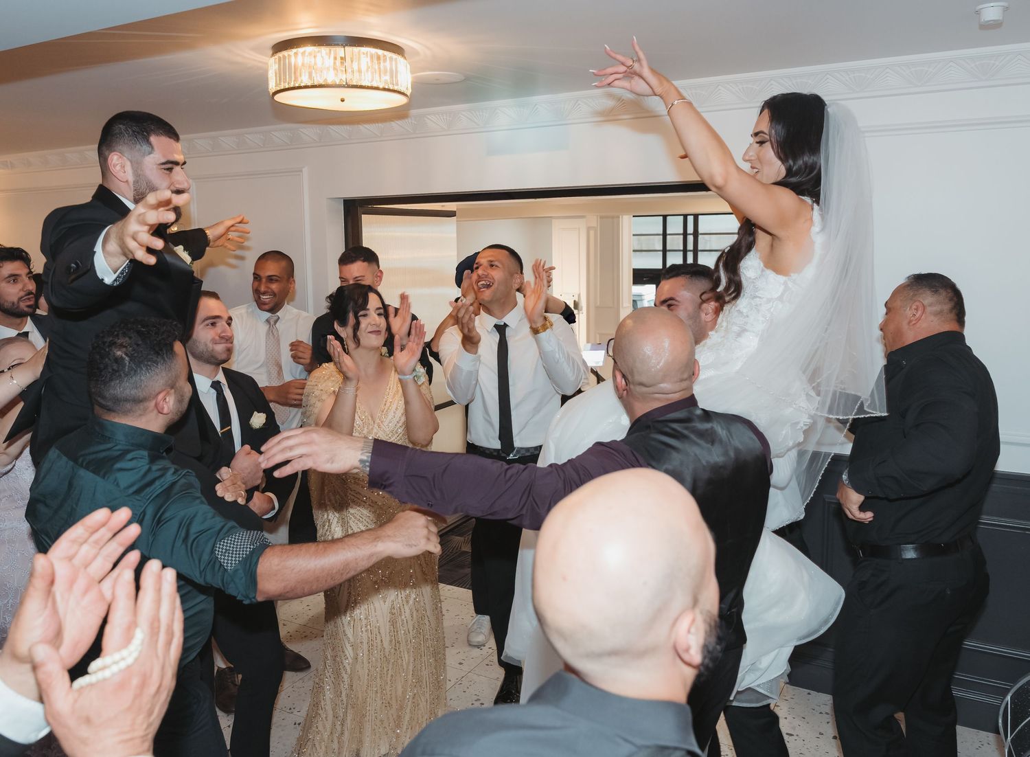 Wedding guests celebrate and dance with enthusiasm during a lively reception in an elegant indoor venue.