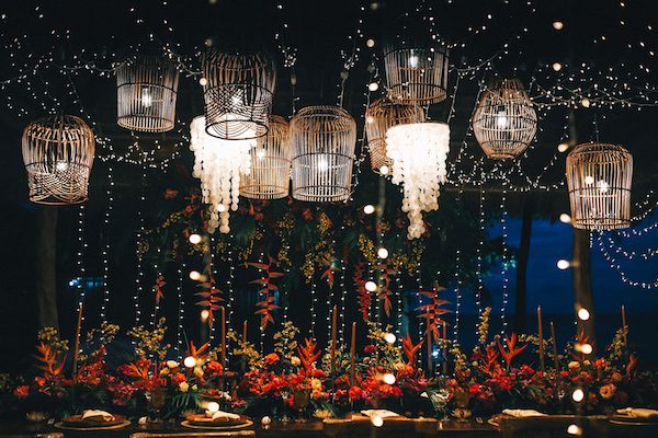 Crystal chandeliers illuminate a romantic setting with red flowers and twinkling lights creating an elegant ambiance.