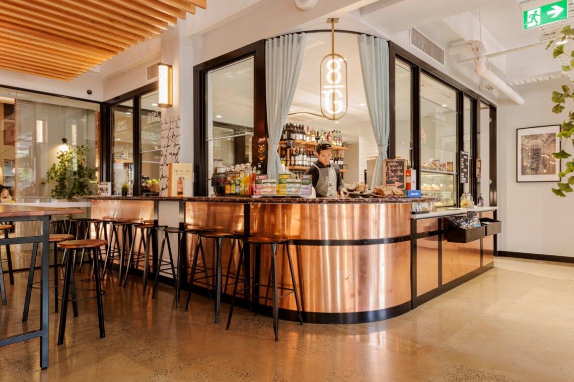 Modern restaurant interior with wood ceiling panels, sleek bar counter, and contemporary dining furniture in warm lighting.