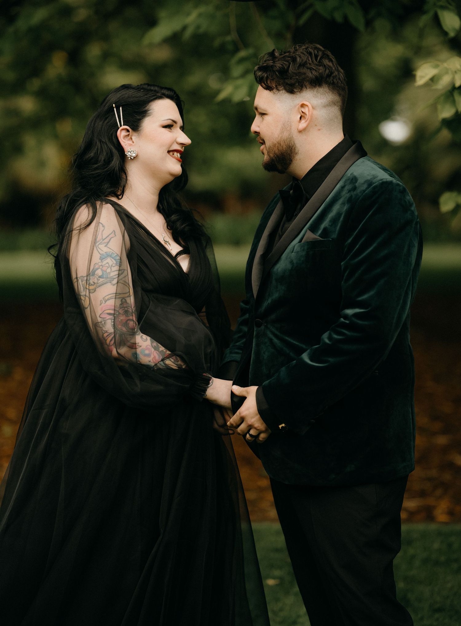 A couple in black attire share intimate moments and laughter during an outdoor autumn photoshoot.