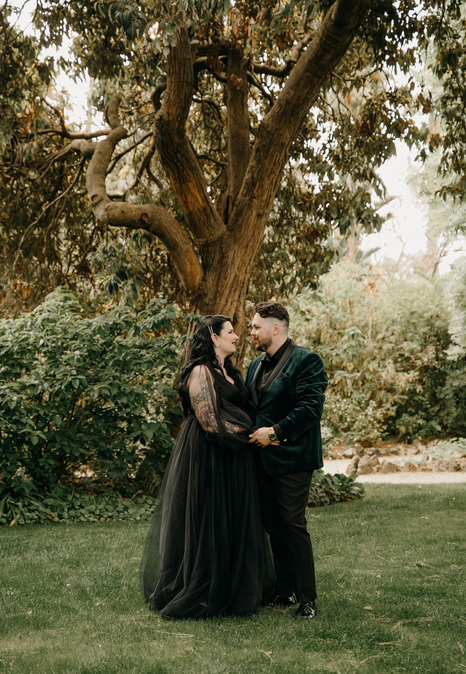 A romantic couple in dark attire share tender moments in a garden setting during a photo sequence.