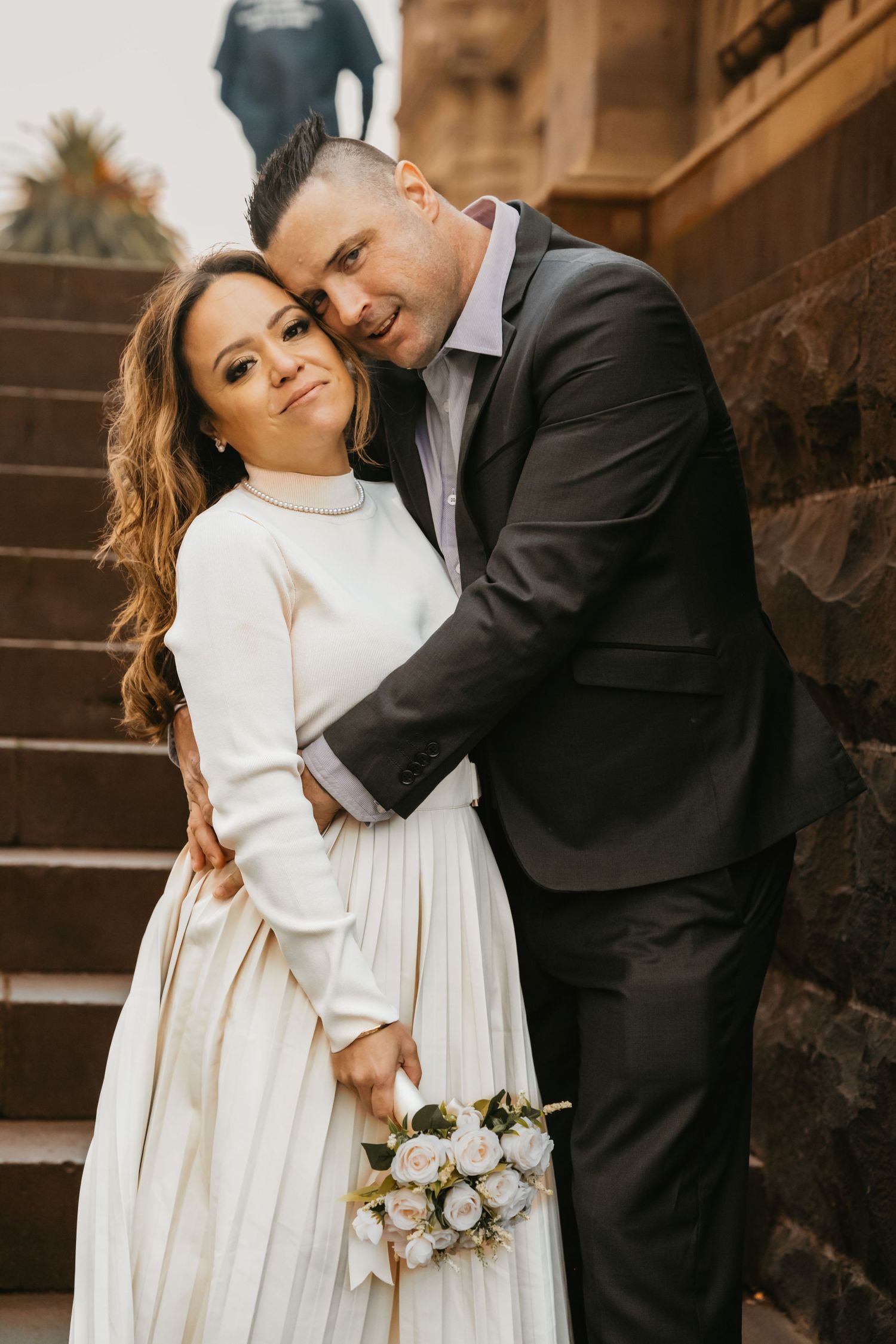 A romantic couple in formal attire share tender moments on rustic wooden stairs in a warm sepia-toned setting.