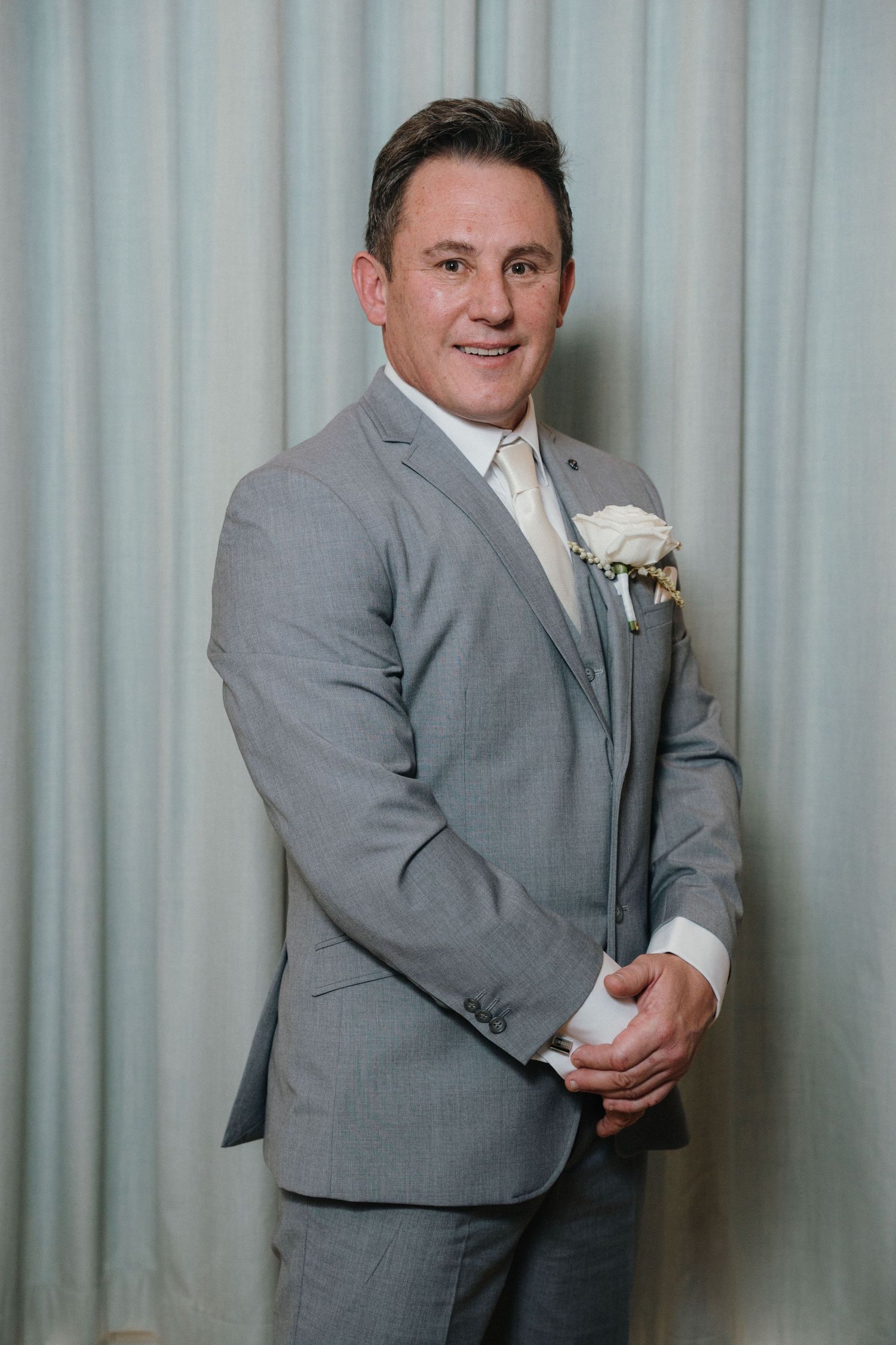A person in a grey suit poses playfully in a sequence of three photos against a light curtain background.