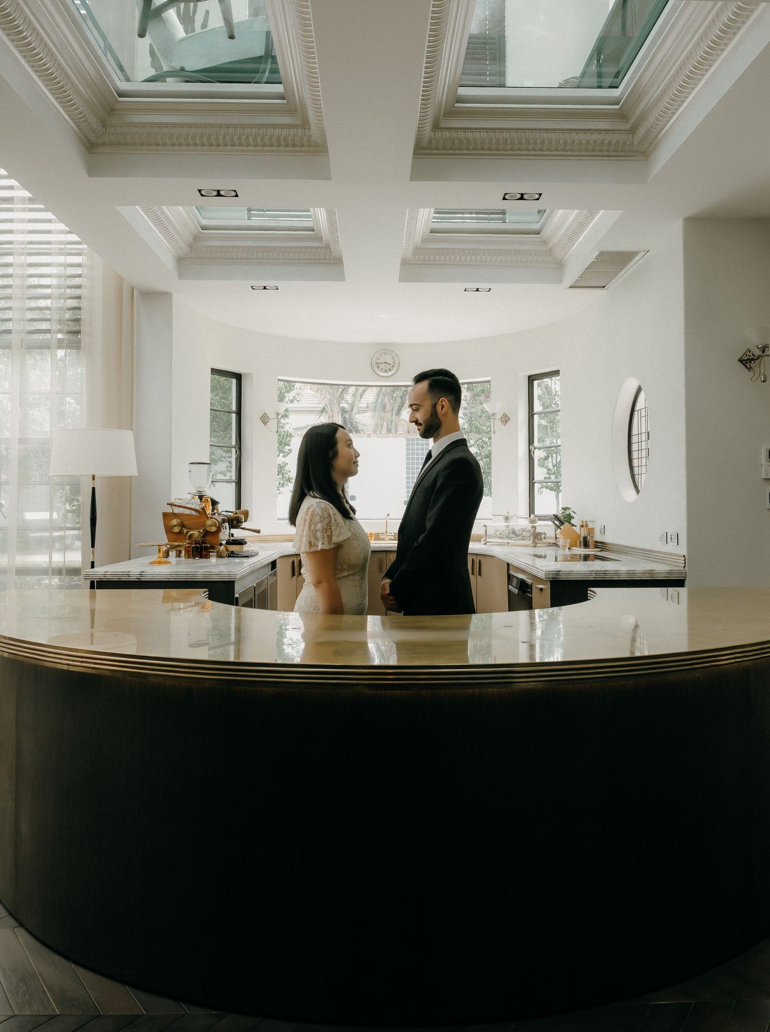 A couple stands together in a bright modern kitchen with skylights and a curved dark counter.