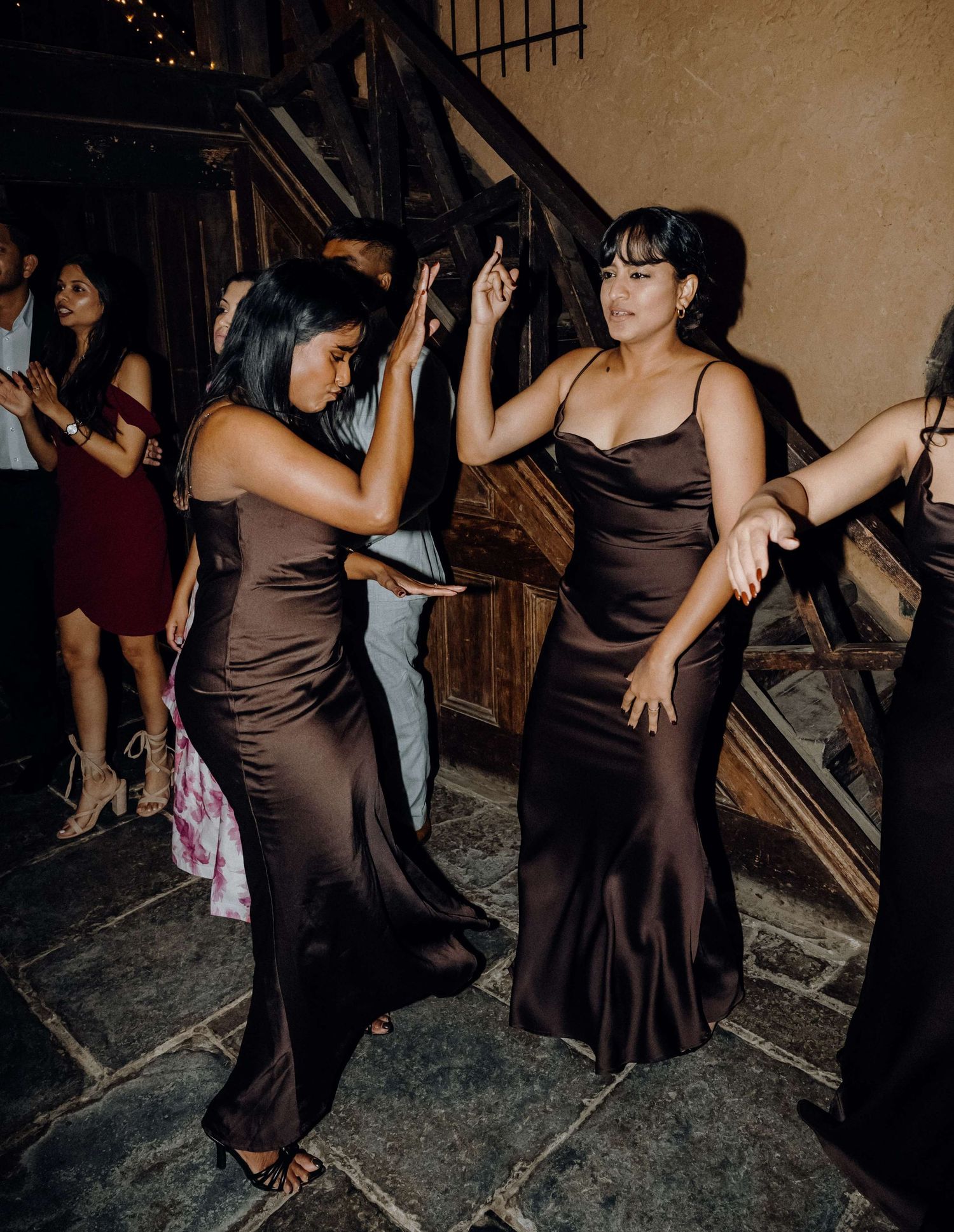 Two women in elegant brown satin dresses dancing together on a dark stone floor at a formal event.
