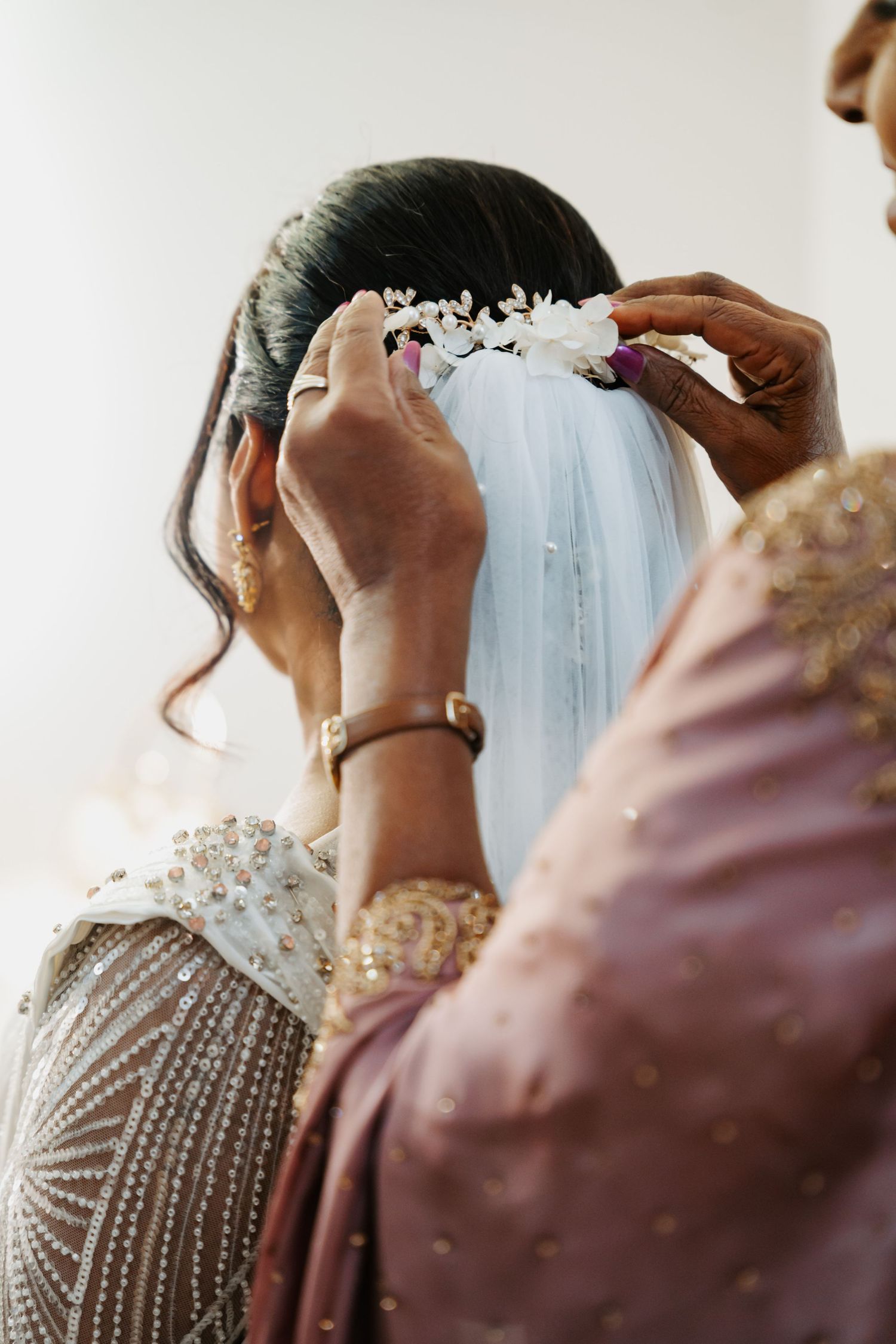 Close-up of hands adjusting details on an ornate pearl-embellished white wedding veil.