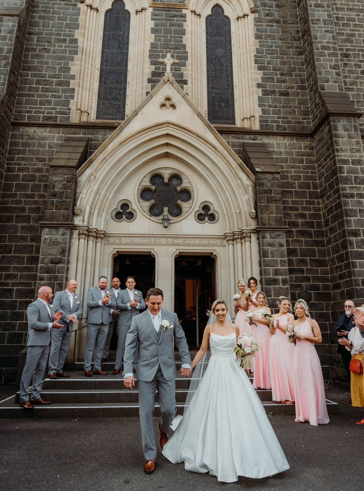 Wedding party poses in front of gothic church entrance with stone archways and decorative details.