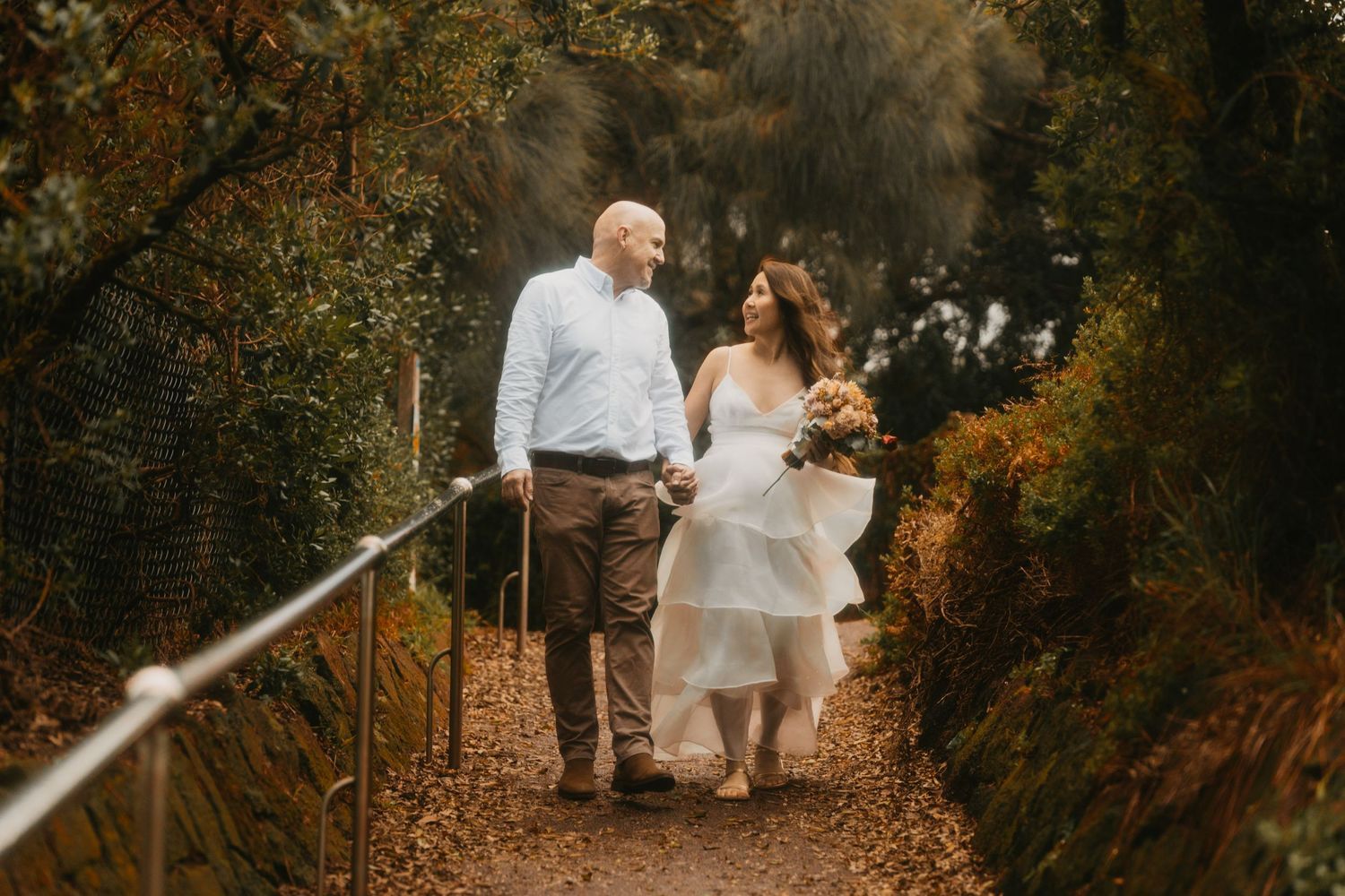 Couple walking hand in hand down a romantic autumn forest path covered in golden fallen leaves.