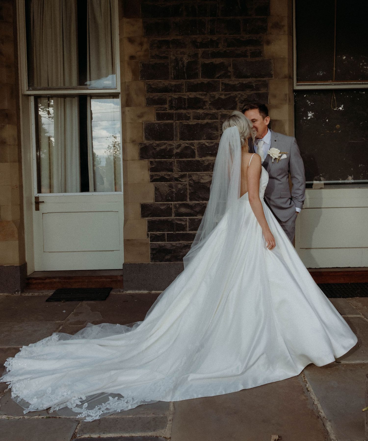 A flowing white wedding dress train trails elegantly across a stone porch with multiple doorways.