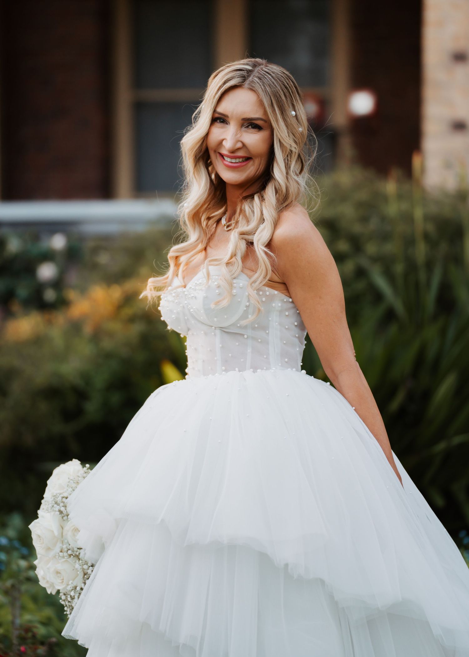A bride in a flowing white tulle wedding dress twirls playfully in a garden setting during a photo session.