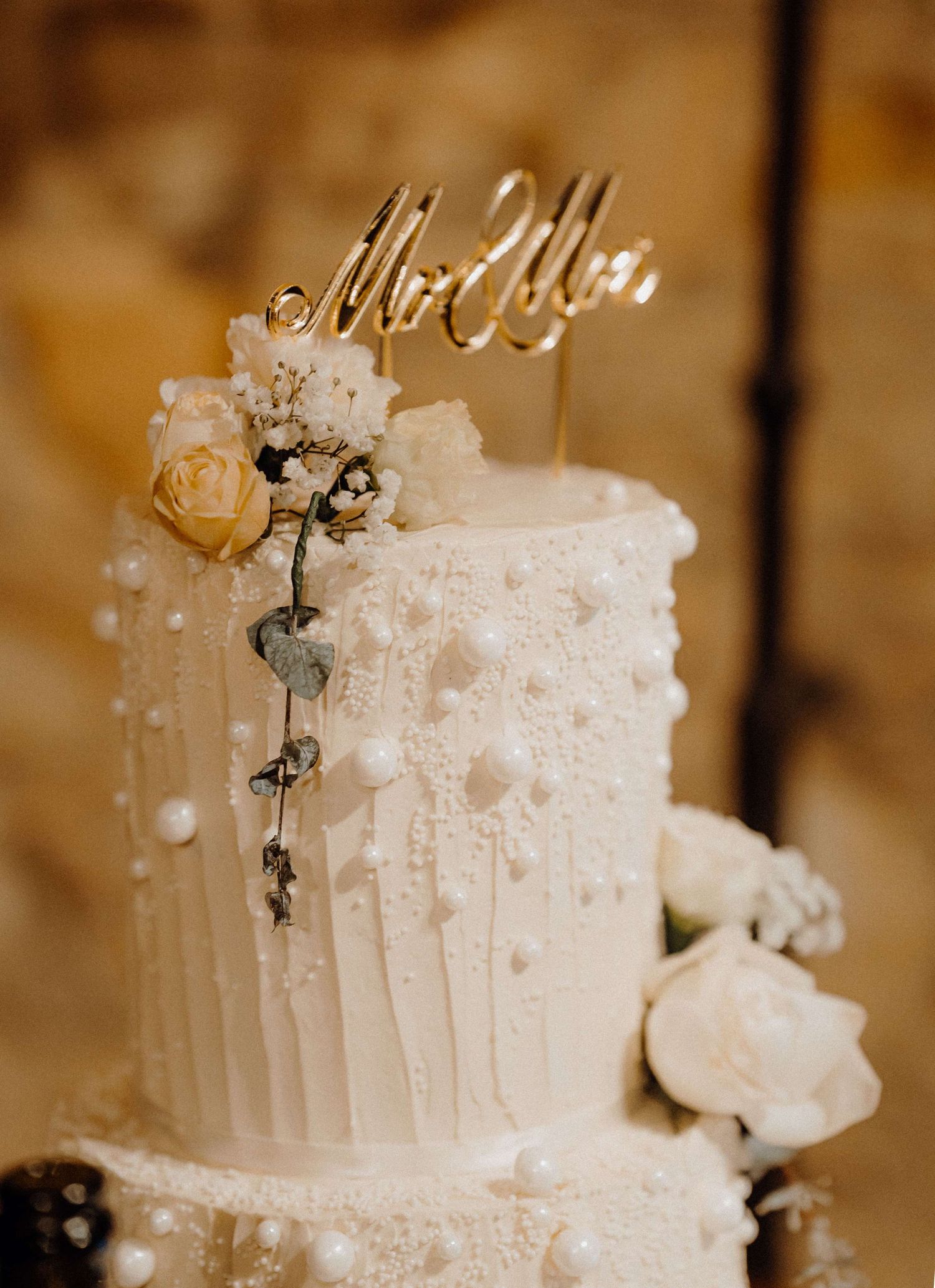 Elegant white wedding cake decorated with pearls, roses and a delicate Mr and Mrs topper in a romantic sepia setting.