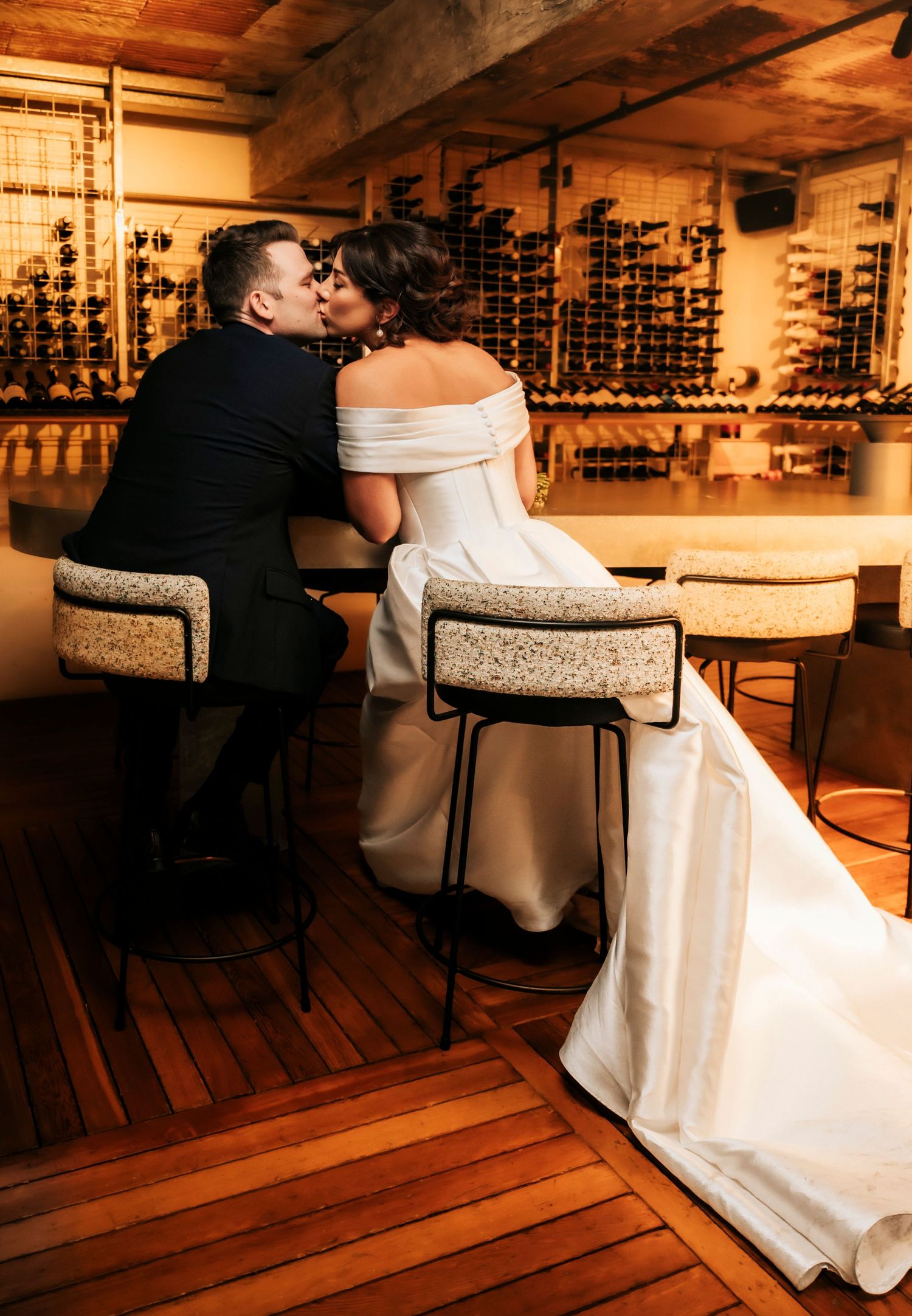A romantic wedding couple shares an intimate moment at a rustic bar with wooden floors and soft lighting.