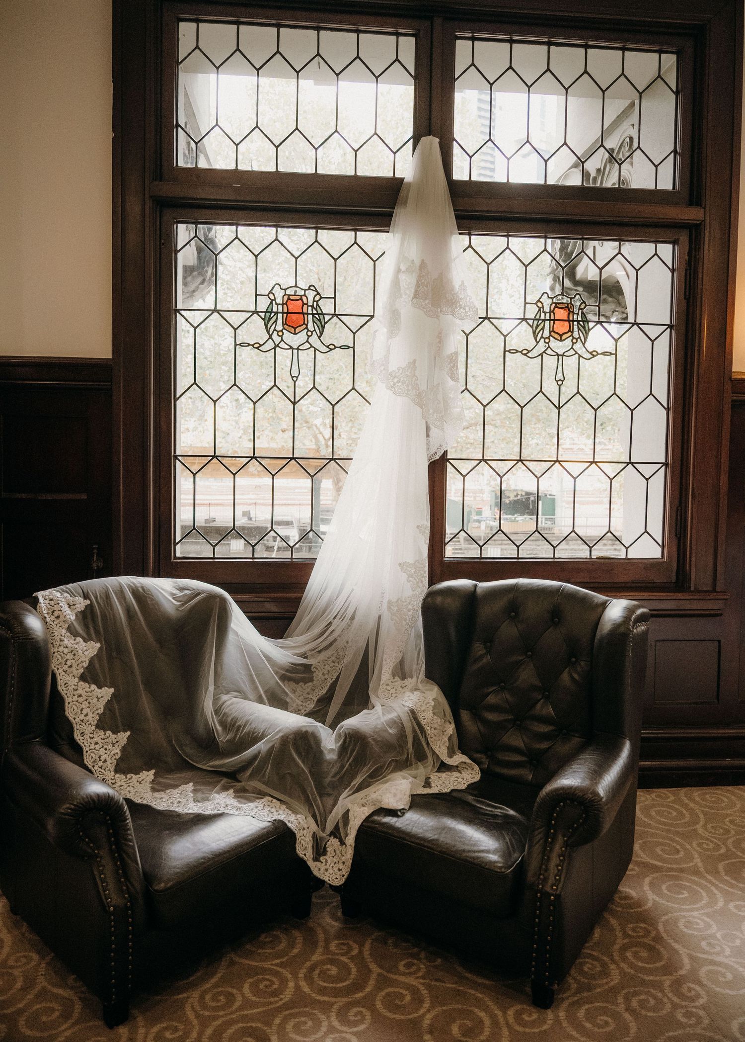 A wedding veil draped over leather chairs before stained glass windows in an elegant venue.