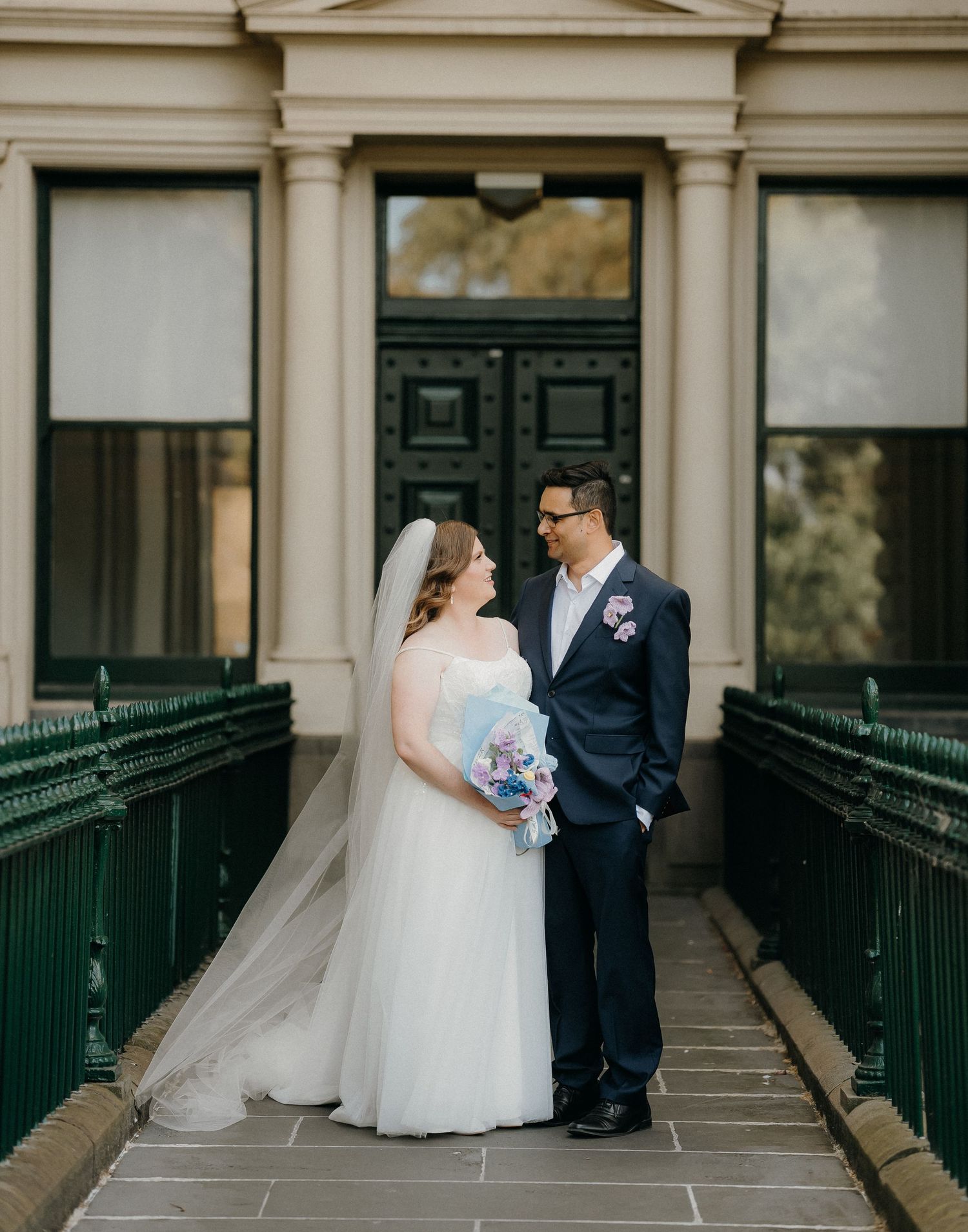 Couple sharing an intimate moment on a covered porch with white columns and green railings.