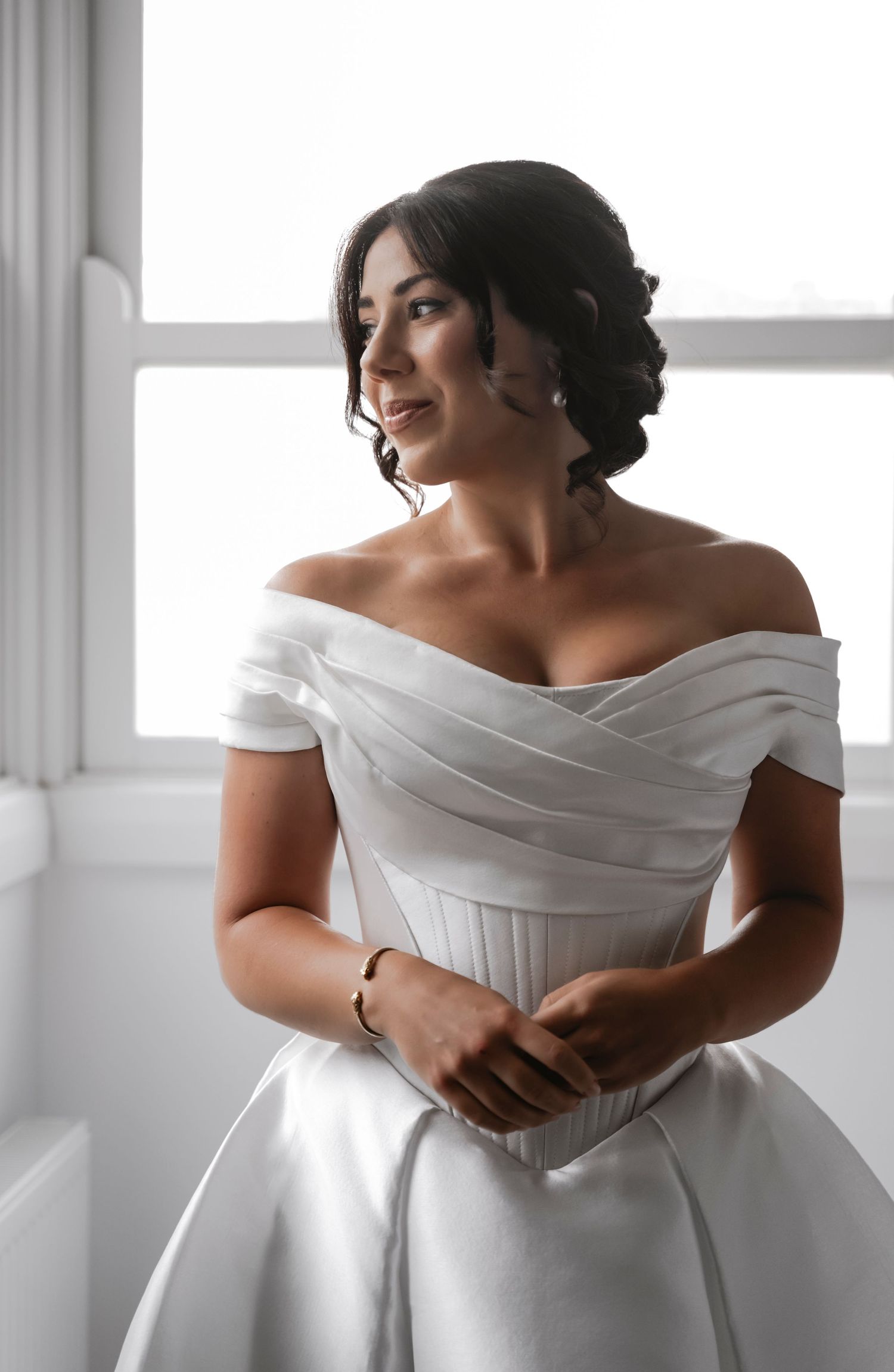 A bride in an elegant off-shoulder white wedding gown poses gracefully near bright windows, shown in multiple angles.