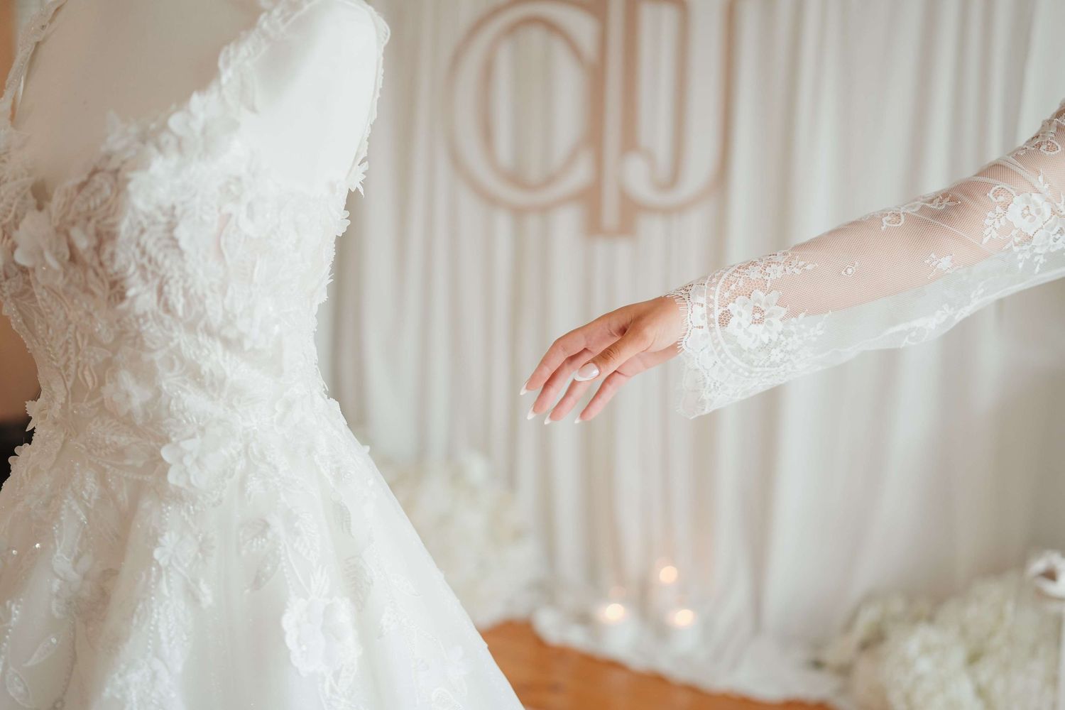 A detailed white lace wedding dress and sleeve against an ivory backdrop.
