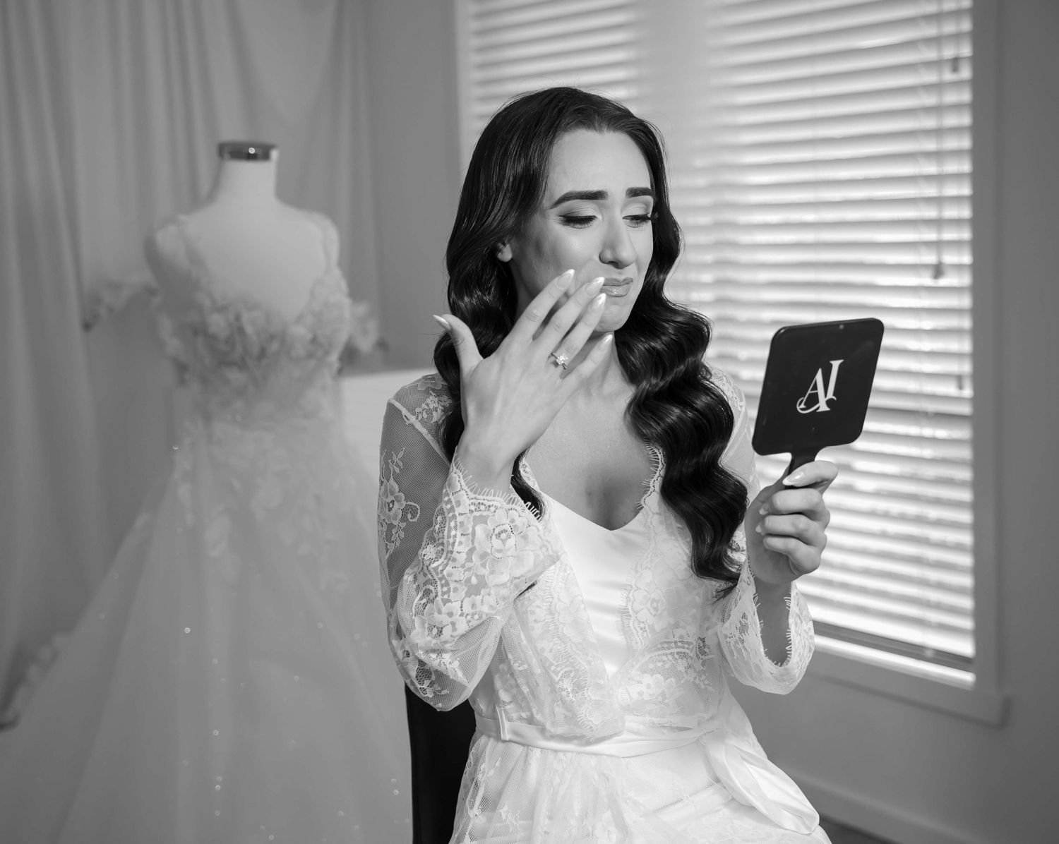 A bride in a white lace wedding dress shows off her gown in a black and white getting ready photo.