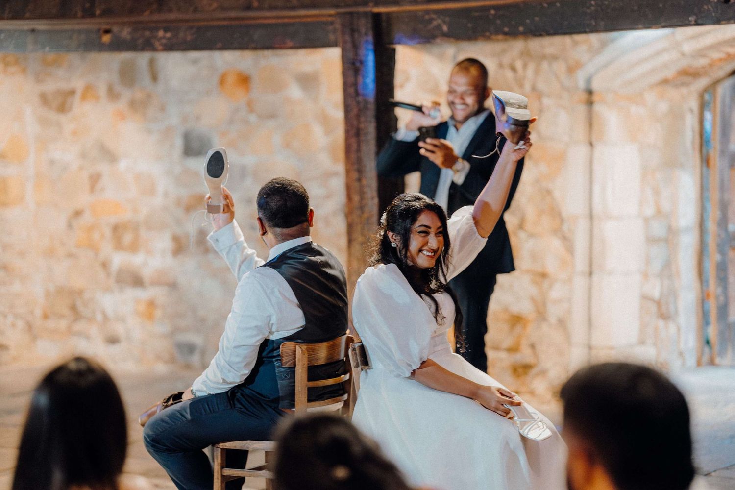 Wedding couple and guests dance together on a rustic venue dance floor during an evening reception celebration.