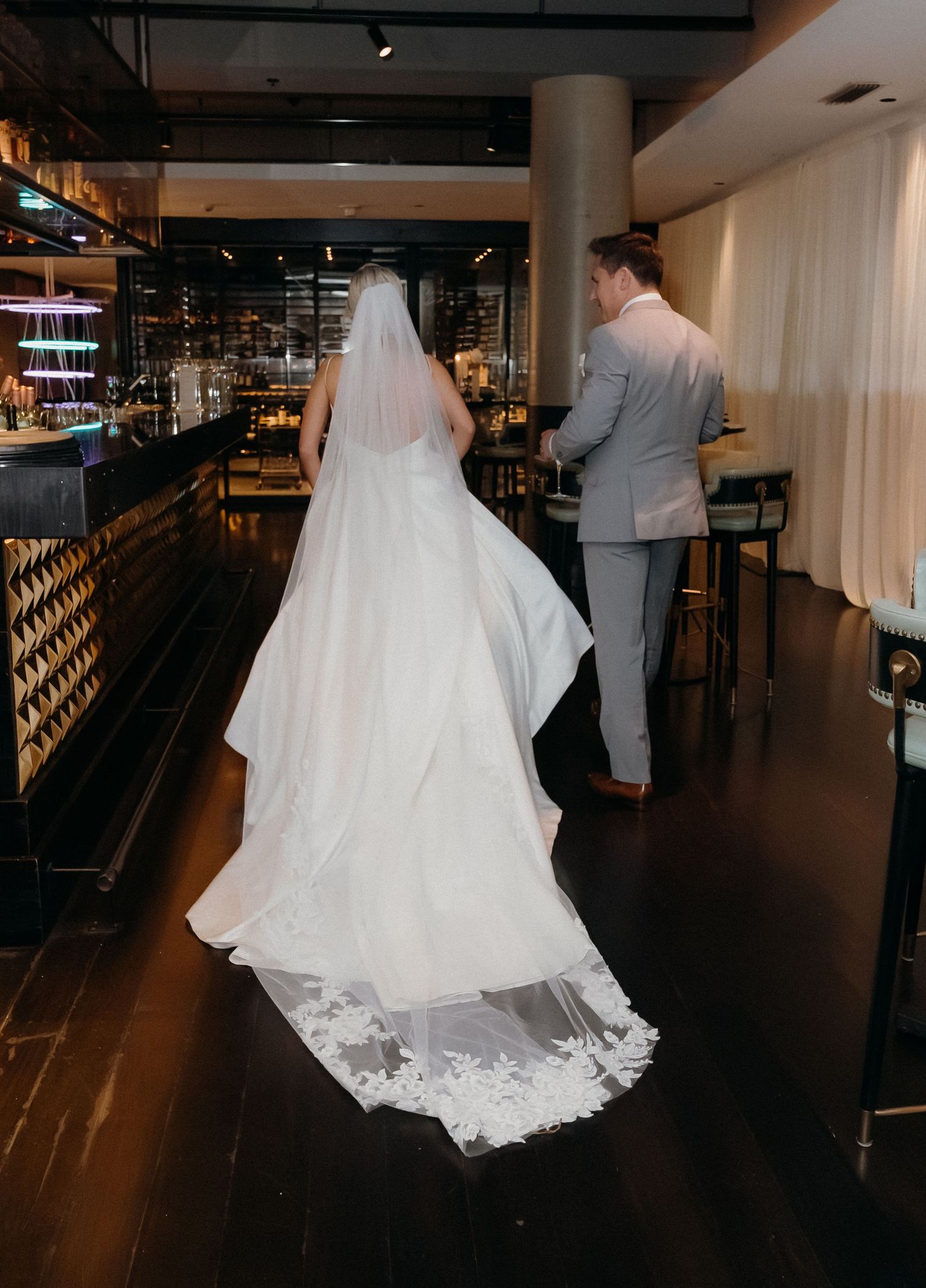 Couple in wedding attire walking through a dimly lit venue with elegant decor and dramatic lighting.