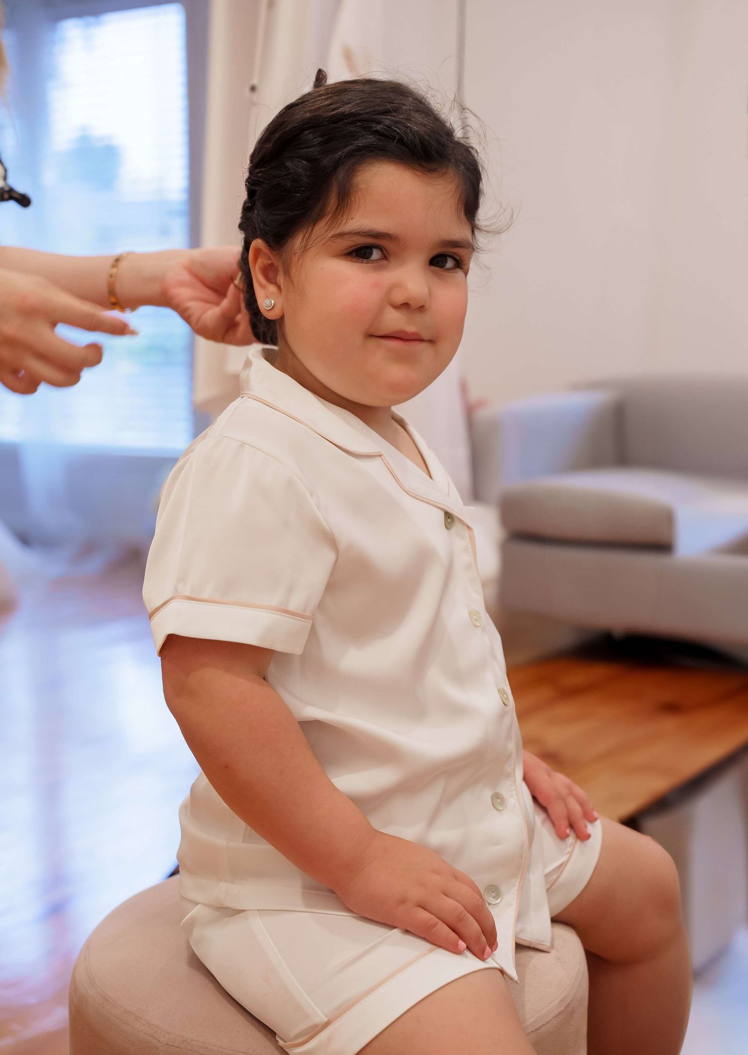 Child wearing white cotton romper outfit sitting on hardwood floor in bright indoor setting.