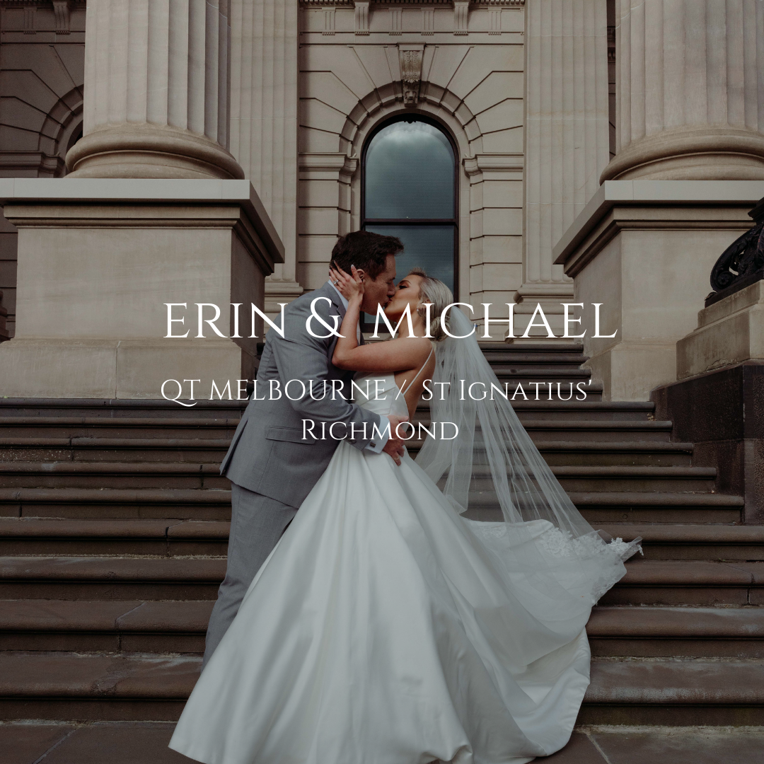 A couple in wedding attire stands between grand stone columns at a historic Melbourne building as a veil flows in the breeze.