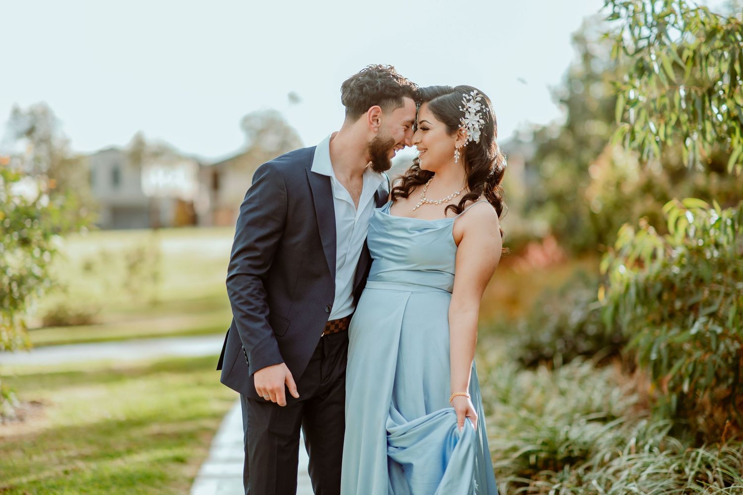 A couple in formal attire shares a romantic moment in a lush garden setting during golden hour.