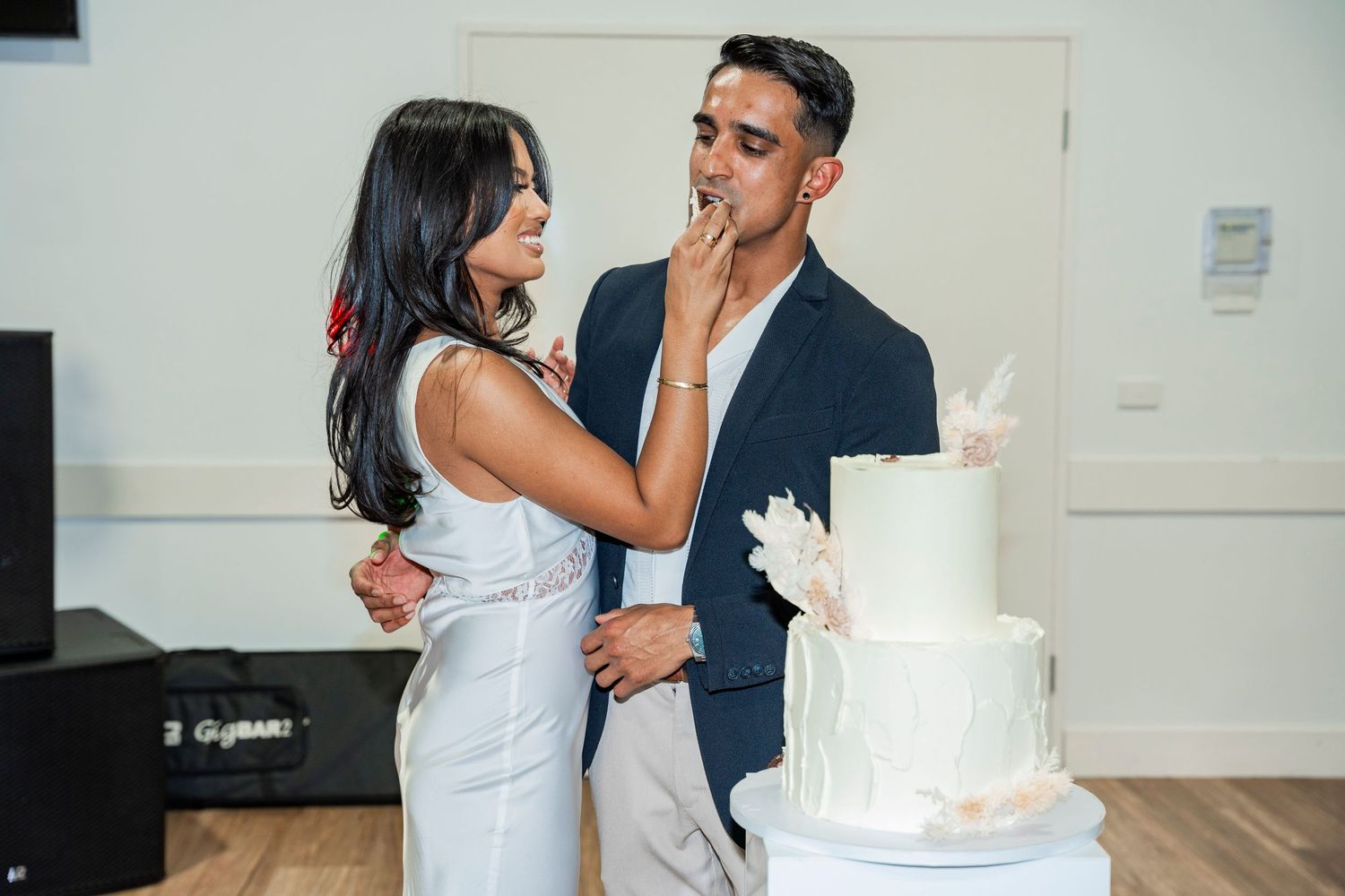 A couple shares a playful moment while feeding each other wedding cake at their reception.