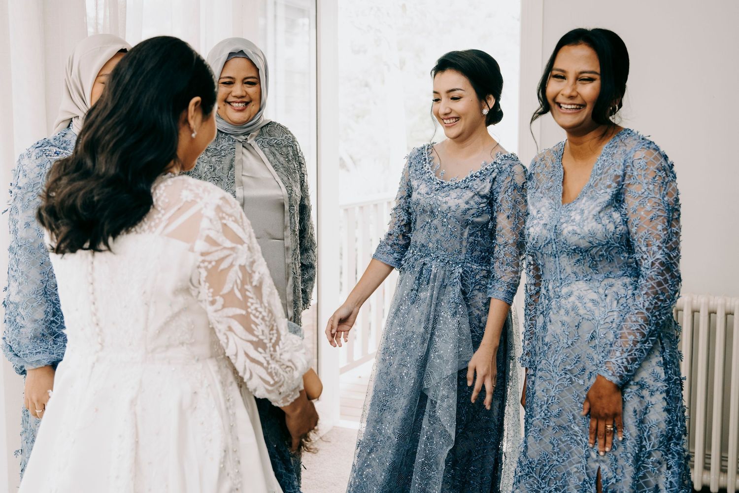 Women wearing coordinated blue and white lace dresses stand together in a bright interior setting.