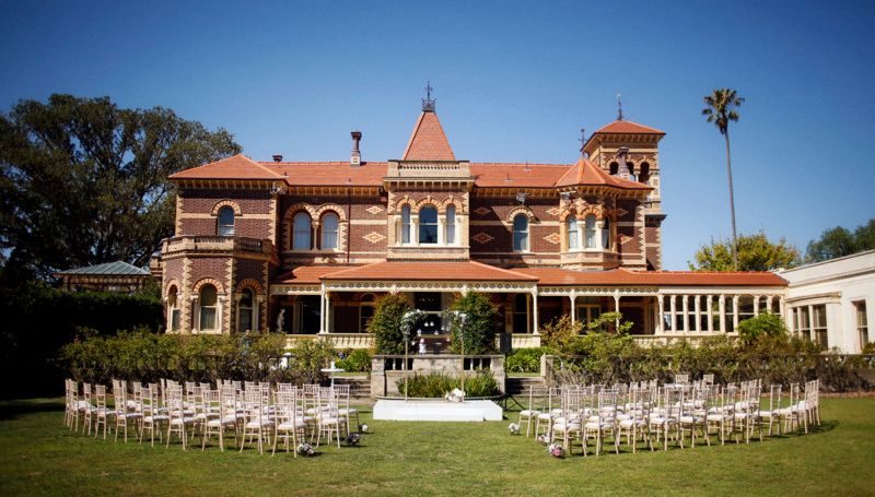 Elegant outdoor wedding venue with Mediterranean-style architecture and rows of white chairs set up on a manicured lawn.