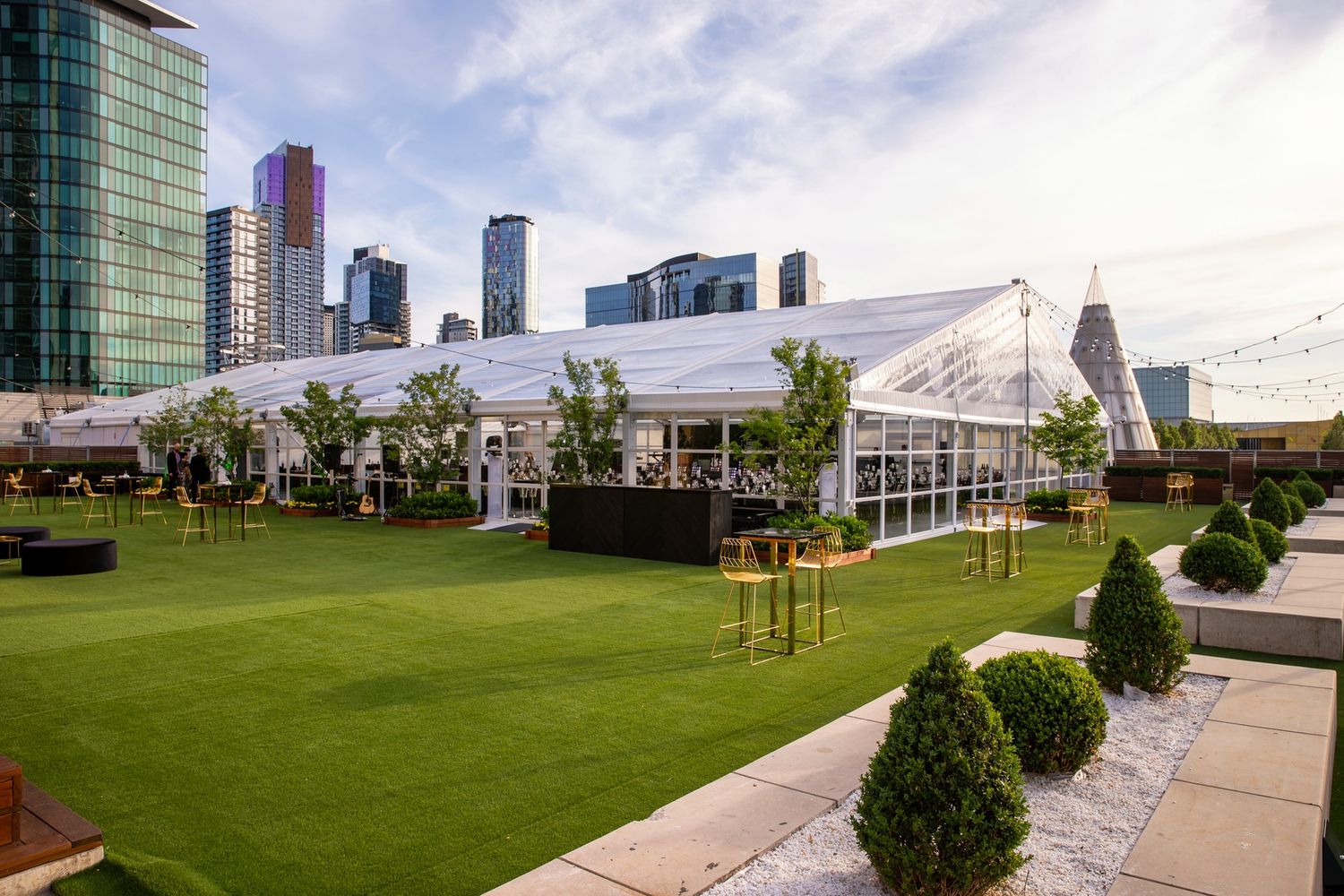 A rooftop garden terrace with green lawn space, trees and city skyline views in the background.