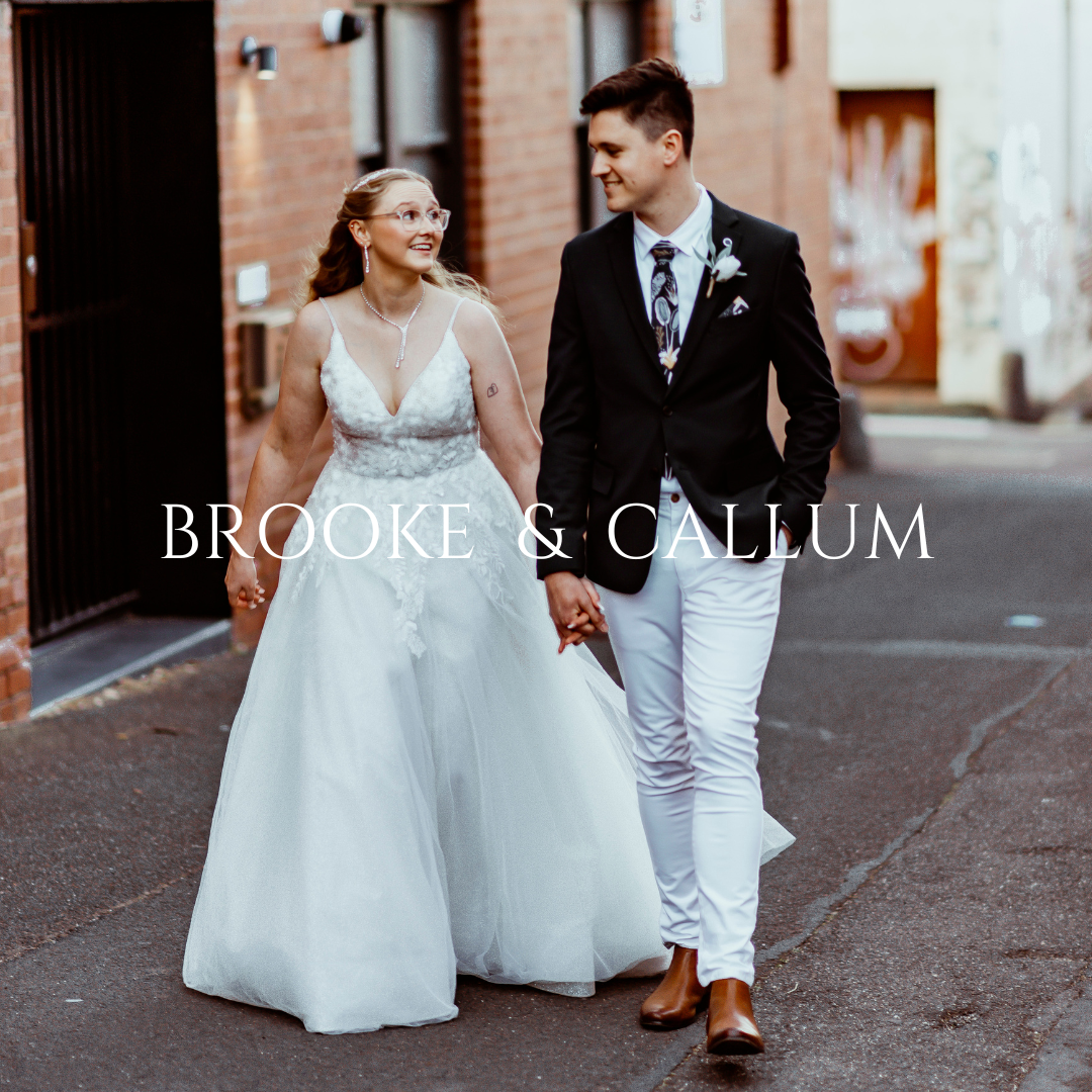 Couple walks hand in hand down urban alley in elegant wedding attire.
