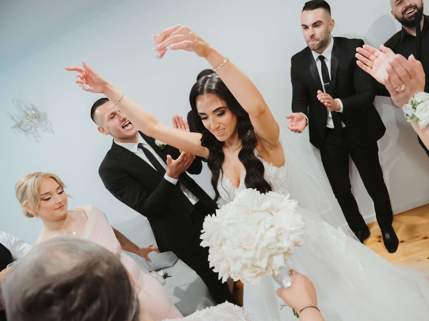 A joyful wedding celebration with people dancing and laughing at an indoor reception venue.