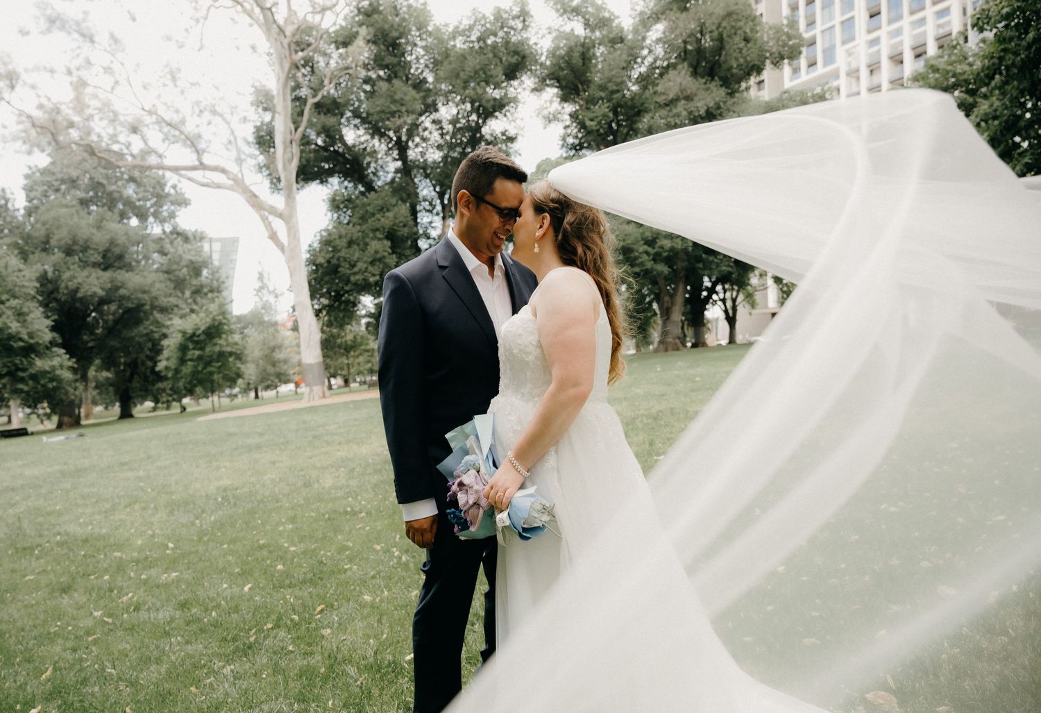A flowing white wedding veil catches the breeze in an outdoor garden setting during a romantic ceremony.