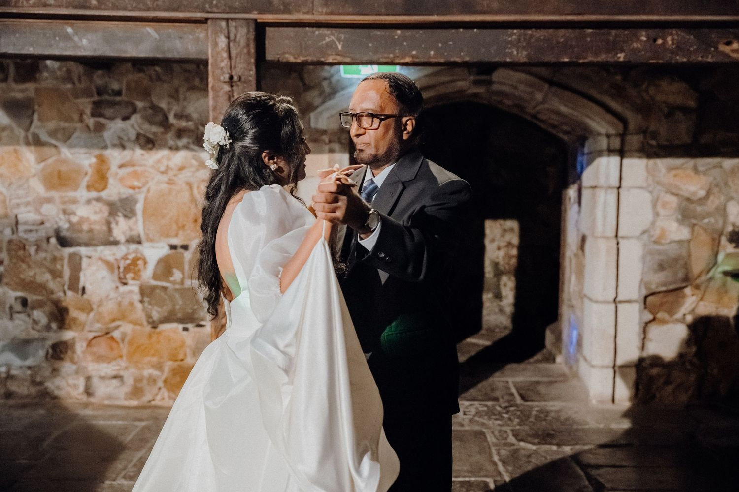A romantic wedding moment captured at a rustic stone venue with elegant lighting and decor.
