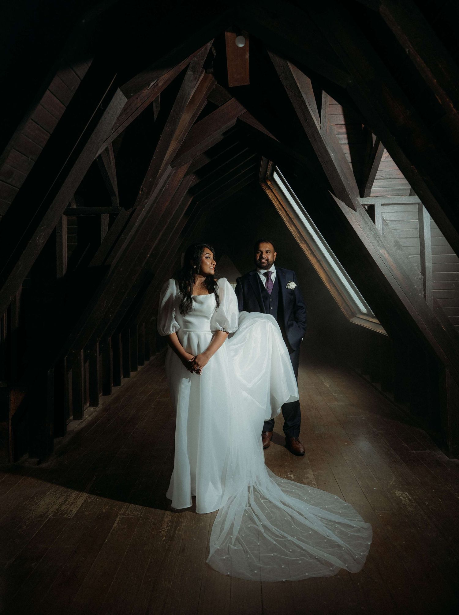 A romantic moment captured in a rustic attic space with dramatic shadows creating an intimate wedding scene.