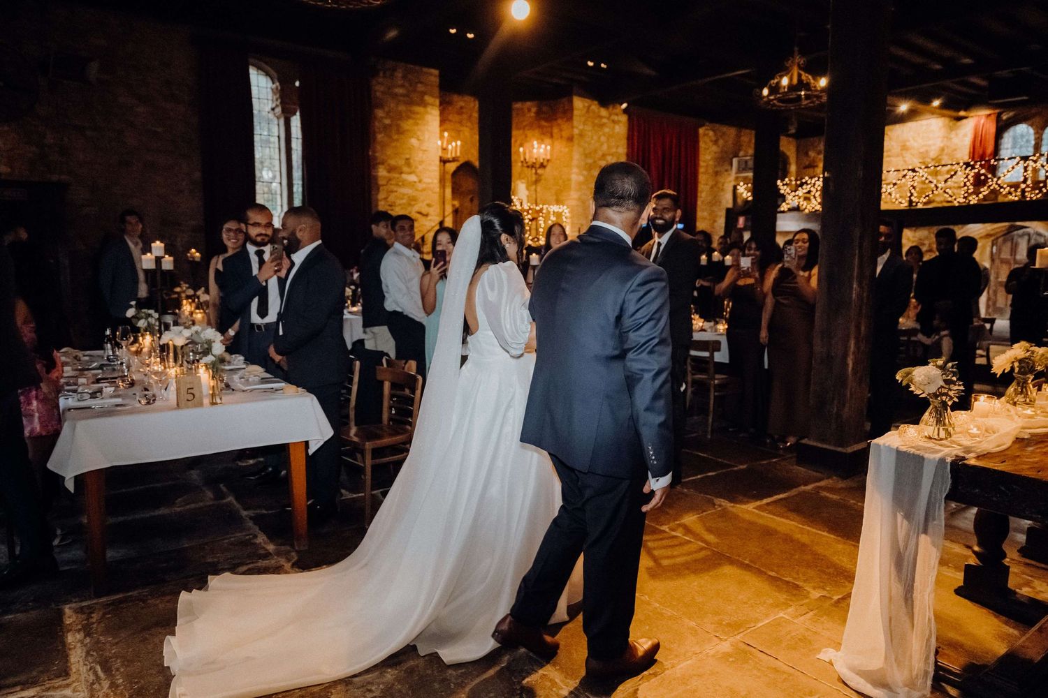 Elegant wedding reception in a rustic brick venue with candlelit tables and flowing white dress.