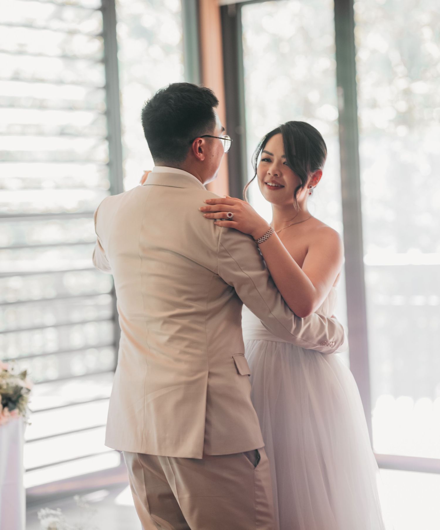 A couple shares their first dance together at a bright indoor wedding venue with sunlit windows.