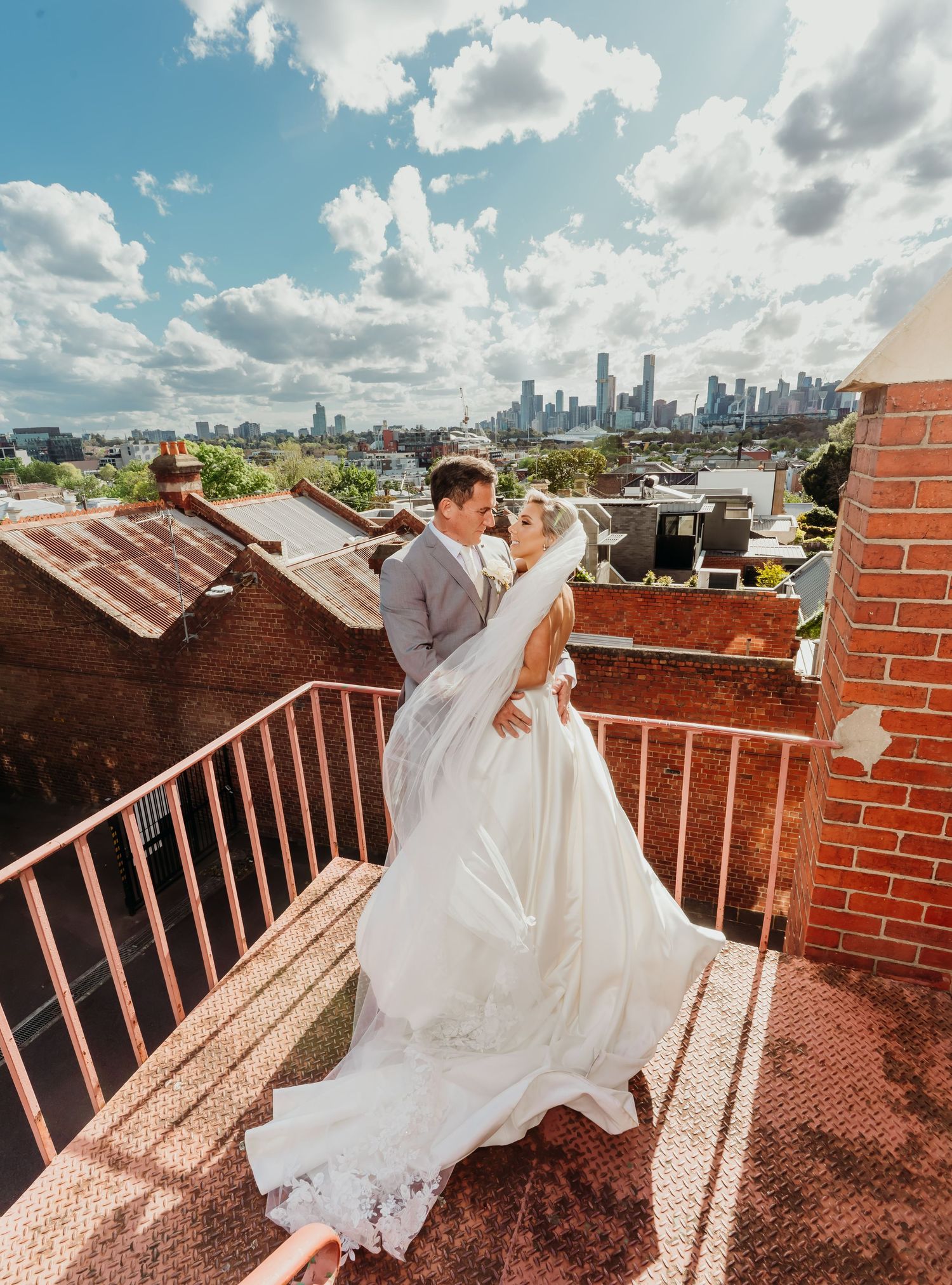 A romantic rooftop wedding photo with the Chicago skyline visible in the background under a bright blue sky with clouds.