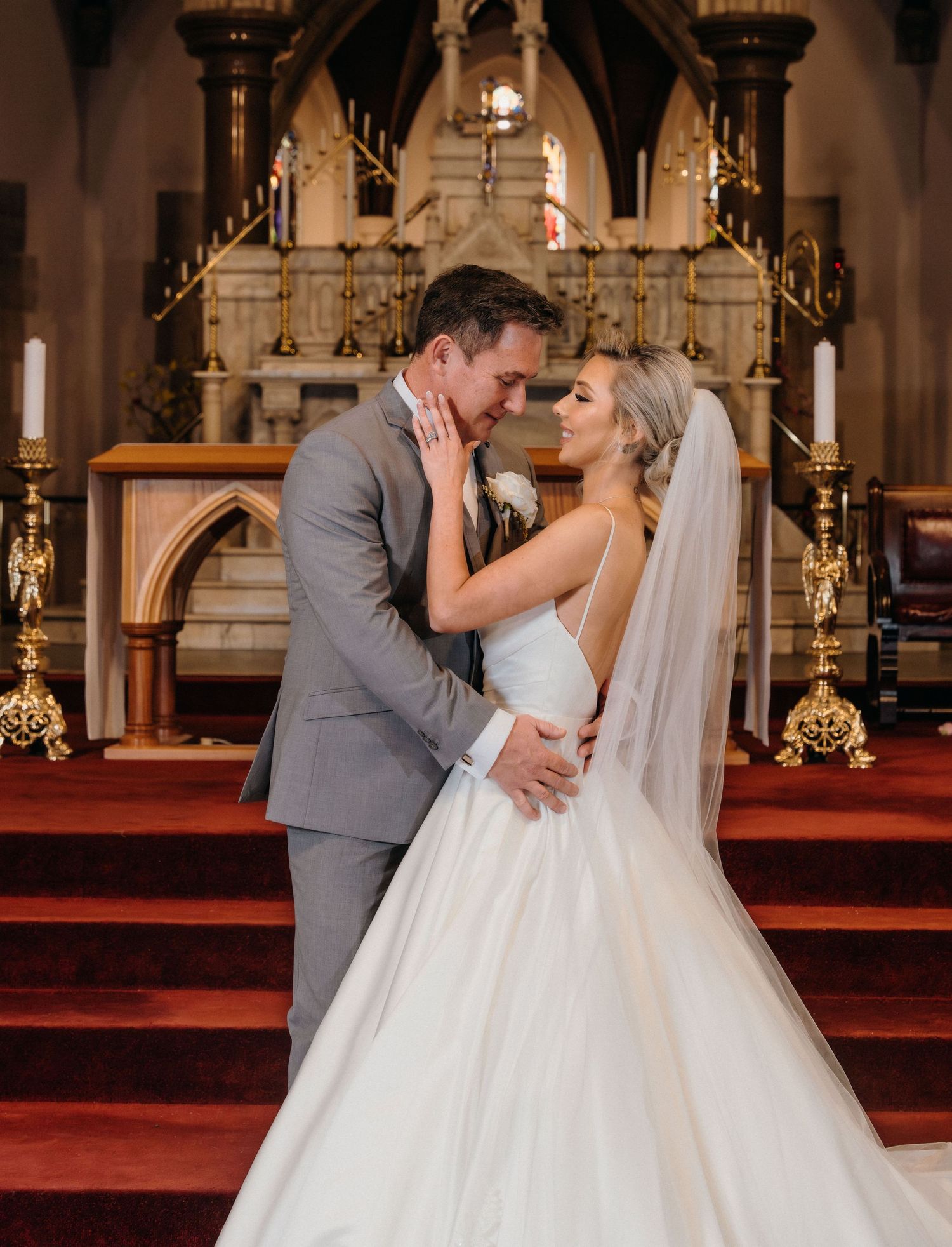 Newlywed couple shares romantic kisses at the altar in an ornate church with red carpet and golden decor.