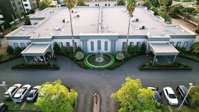 Aerial view of a white Mediterranean-style building with circular driveway and symmetrical palm trees in Miami.