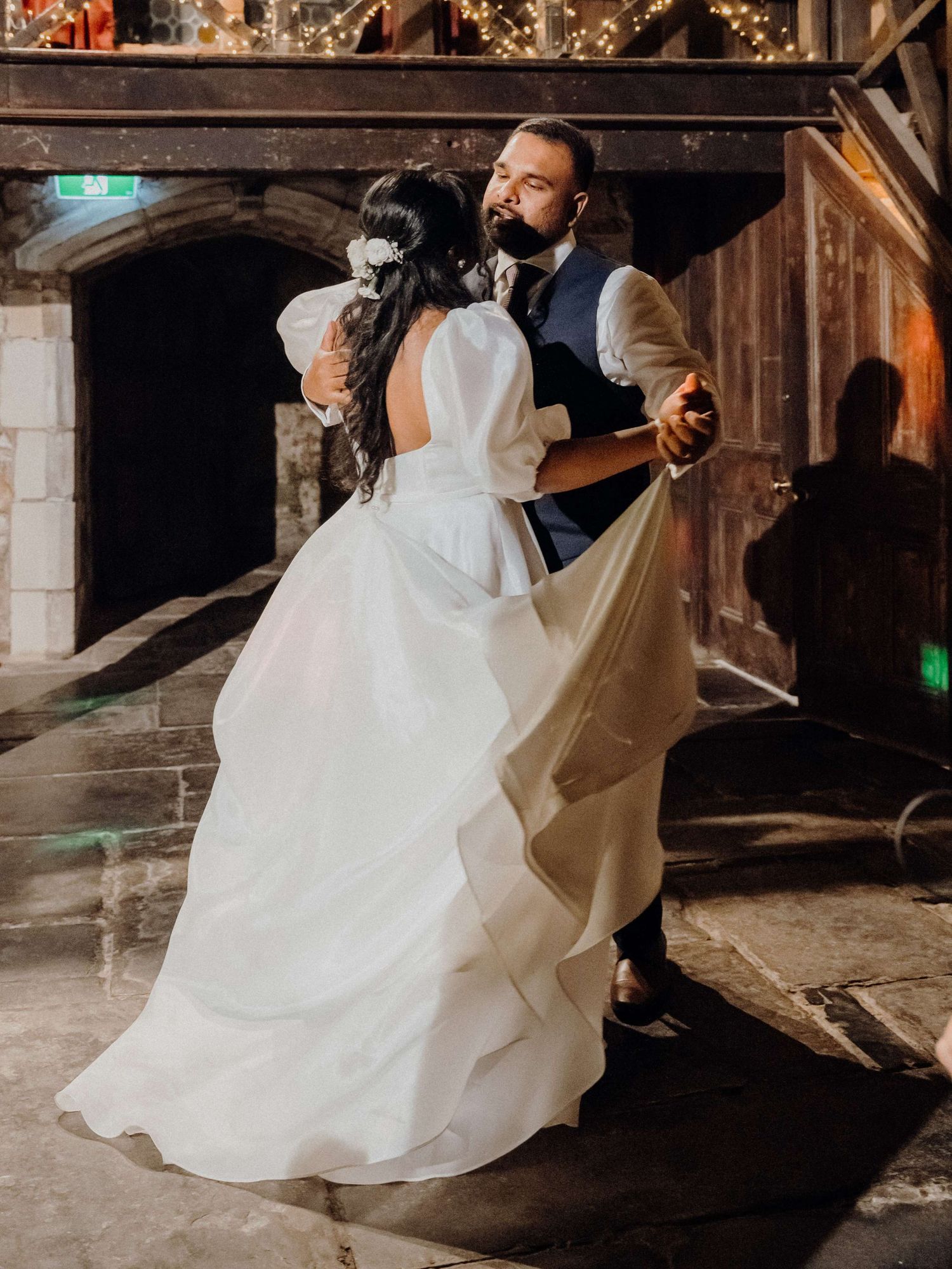 A couple in formal wedding attire dancing intimately in a rustic barn venue with soft lighting and wooden beams.