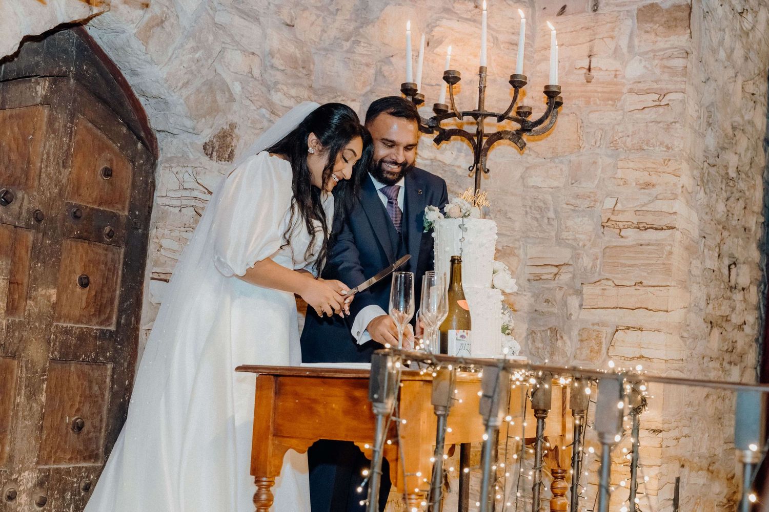 Wedding guests dancing and celebrating in a rustic brick-walled venue with elegant chandelier lighting.
